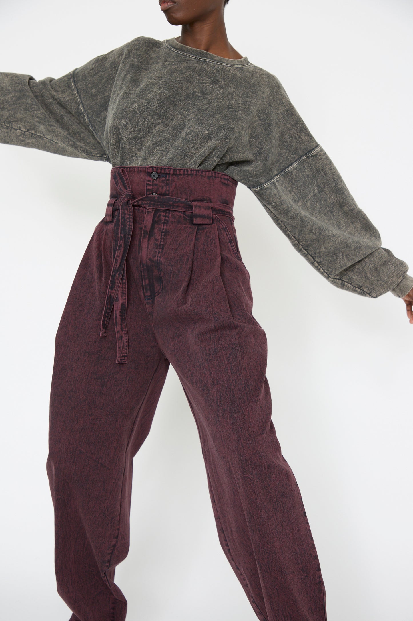 A woman is wearing a gray oversized sweater and the Rachel Comey Acid Madrona Denim Bowman Pant in Boisonberry, with a self-tie belt, while standing in a dynamic pose against a white background.