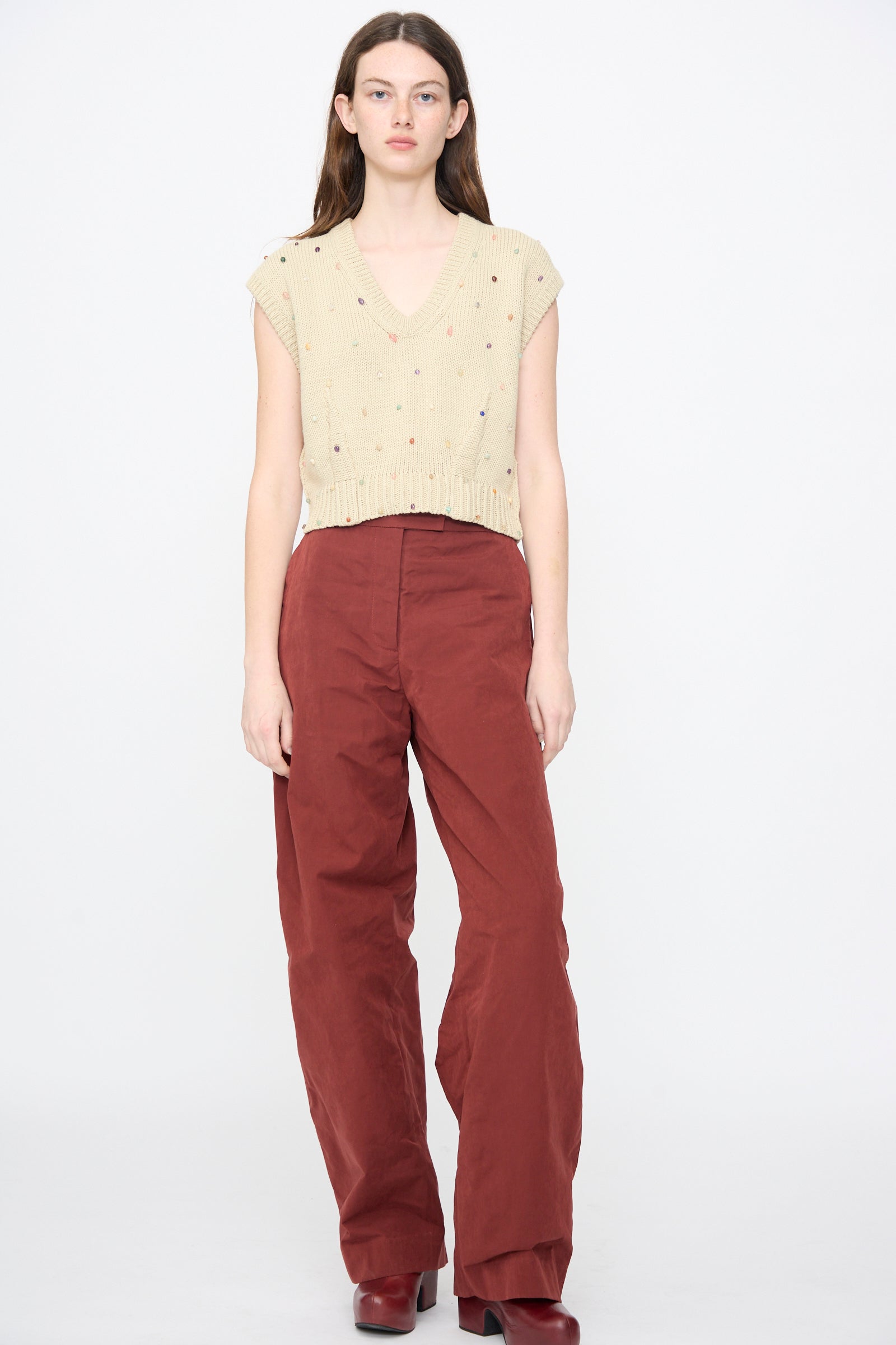 A woman faces forward in the Rachel Comey Acrea Top in Dove, paired with high-waisted, loose maroon pants and matching maroon shoes, set against a plain white background.