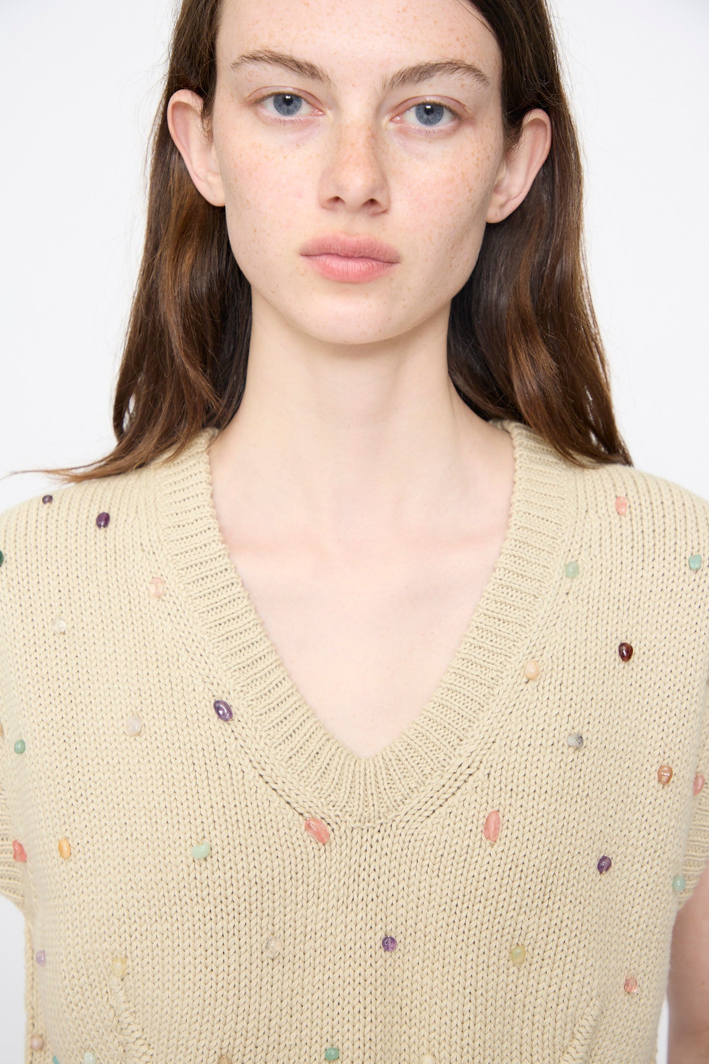 A person with long brown hair wears the Rachel Comey Acrea Top in Dove, a beige chunky knit vest with small colorful embroidered dots, facing forward against a plain background.