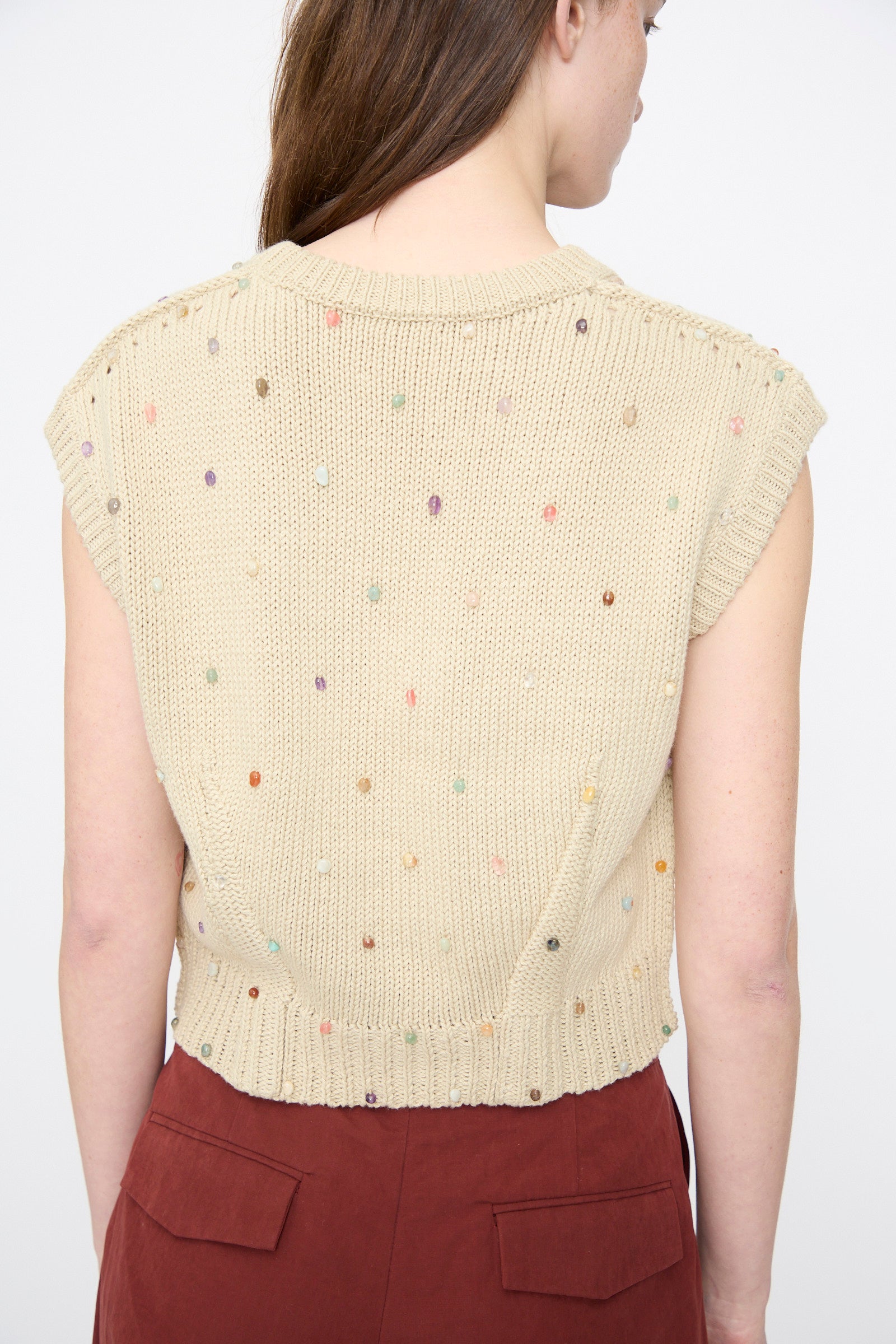 A woman shown from the back wears the Rachel Comey Acrea Top in Dove, a chunky knit vest with multicolored speckles, paired with high-waisted, rust-colored pants.