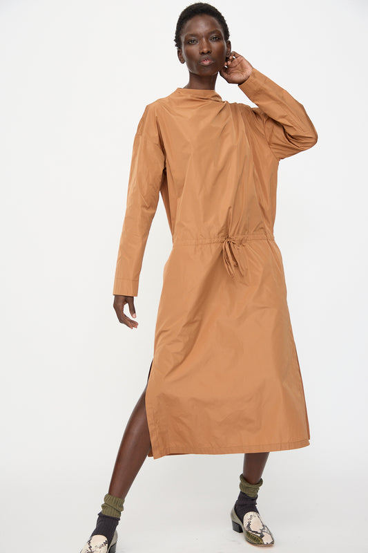 A person models the Rachel Comey Alberry Dress in Copper—a long sleeve midi dress with a drawstring waist made from recycled polyester—standing in a neutral pose against a plain white background.