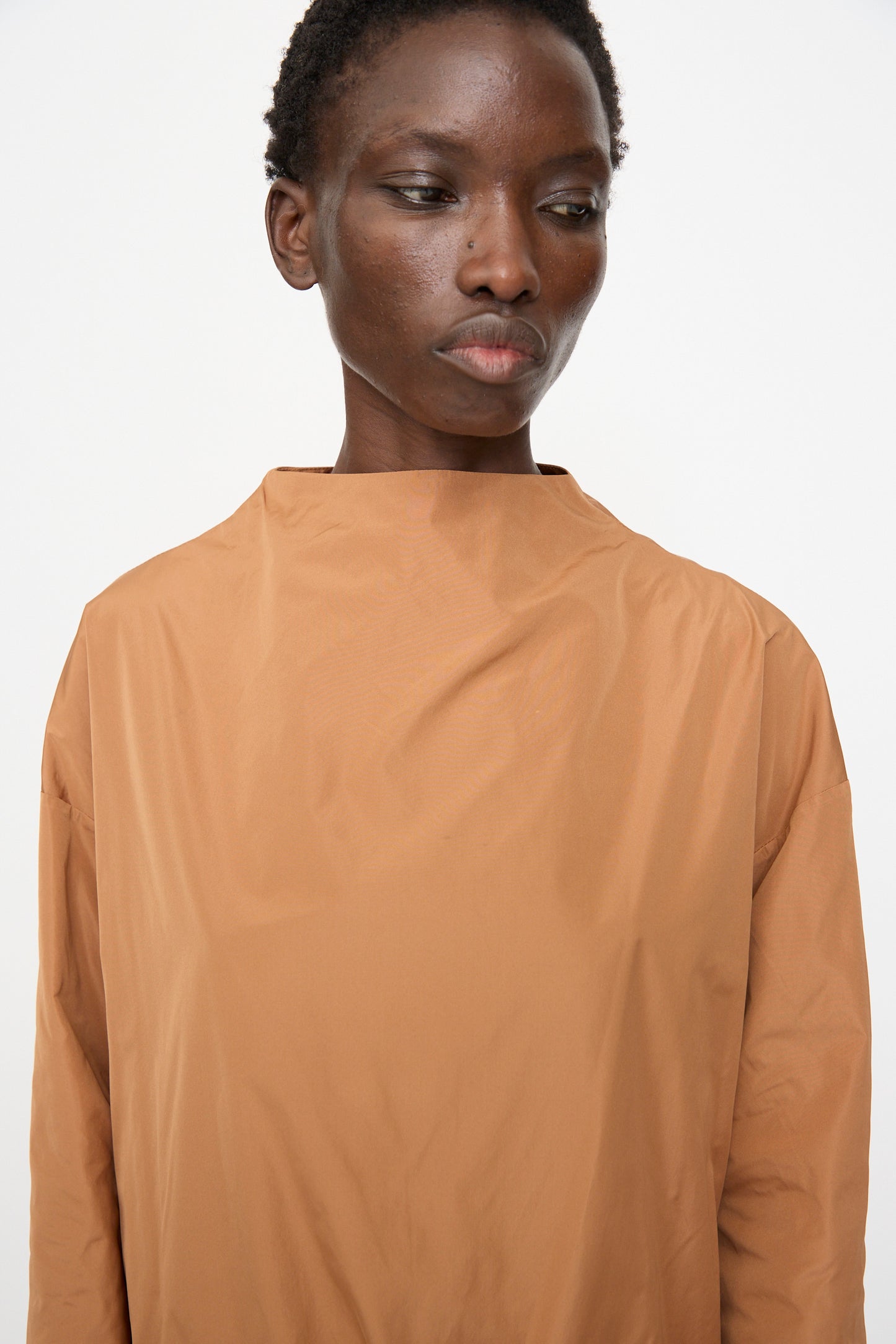 A person with short hair models the Rachel Comey Alberry Dress in Copper, a loose-fitting piece, standing against a plain white background and looking slightly downward.