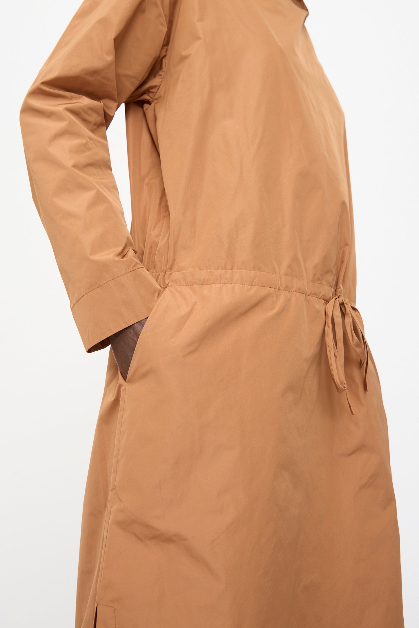 A person wears the Rachel Comey Alberry Dress in Copper, a long sleeve, water-resistant taffeta midi with a drawstring waist and side pocket.