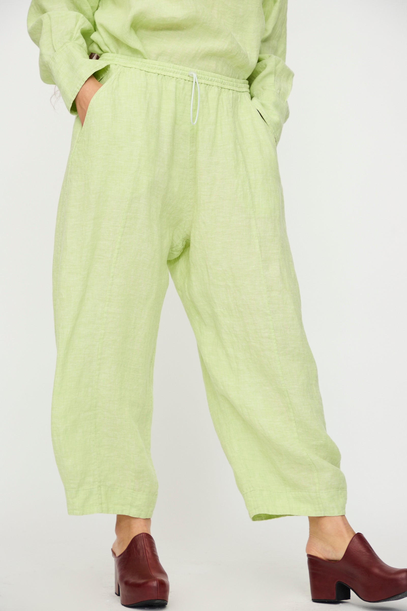 A person wears the Rachel Comey Ashbolt Pant in White Sage, a loose wide-leg style, paired with a matching textured top and brown heeled clogs, standing against a plain background with hands in pockets.