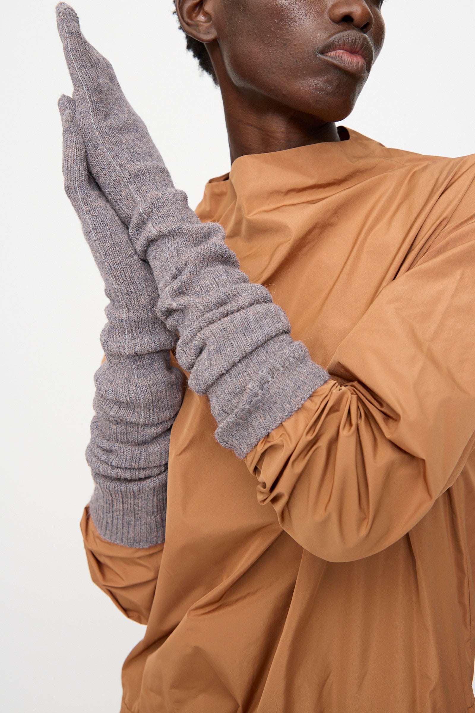 A person wears a tan long-sleeved top and Rachel Comey's Baalam Gloves in Dusty Mauve, made in Peru, holding their hands together against a plain background.