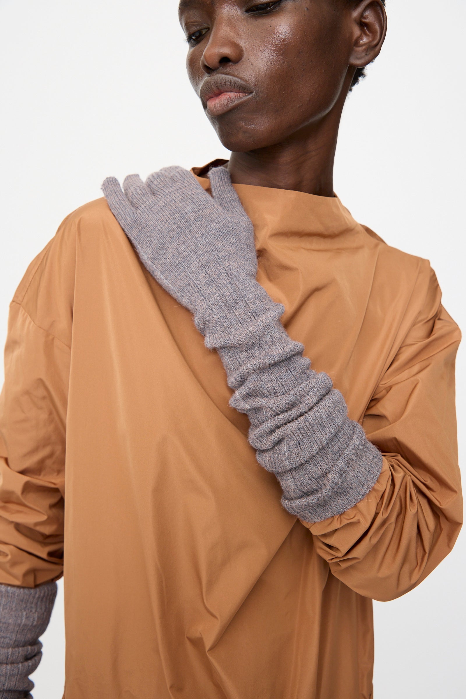 Person wearing a loose tan top and long, ribbed Rachel Comey Baalam Gloves in Dusty Mauve, with one arm crossed and touching their opposite shoulder.