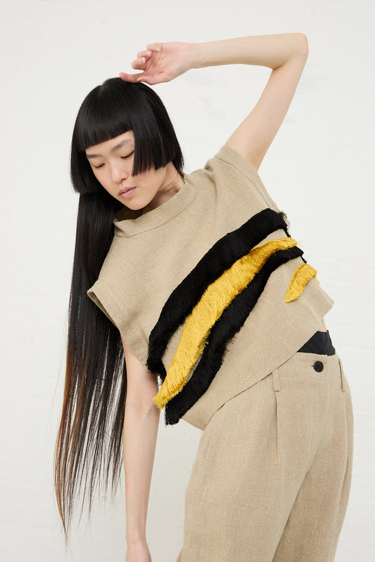 Woman posing in a beige textured linen outfit with black and yellow abstract embroidery, showcasing a unique sleeveless crop top (Bacchus Top in Natural by Rachel Comey) and trousers against a white background.