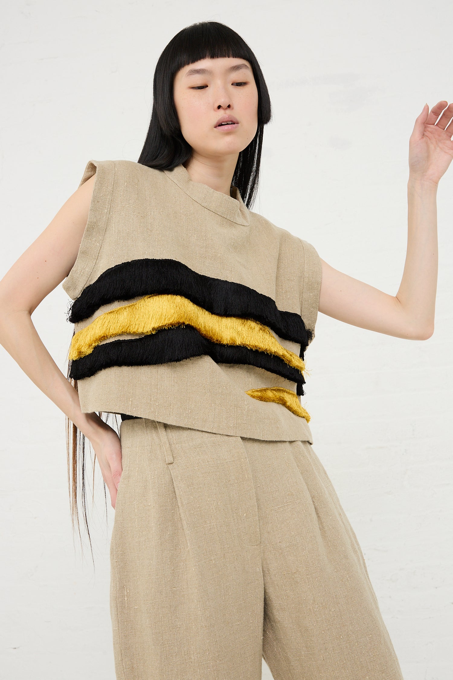 Woman modeling a Rachel Comey Bacchus Top in Natural, a beige sleeveless crop top with black and yellow horizontal stripes, paired with matching trousers, against a white background.