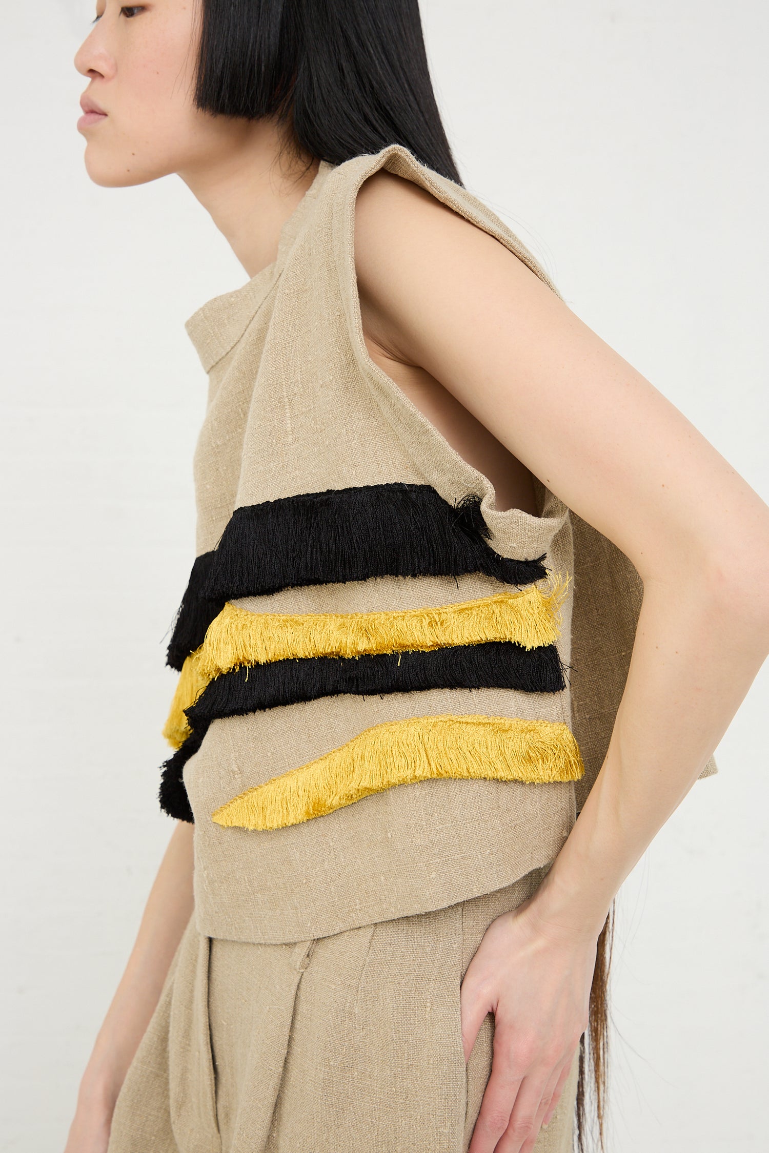 Woman modeling a Bacchus Top in Natural by Rachel Comey with black and yellow fringe details.