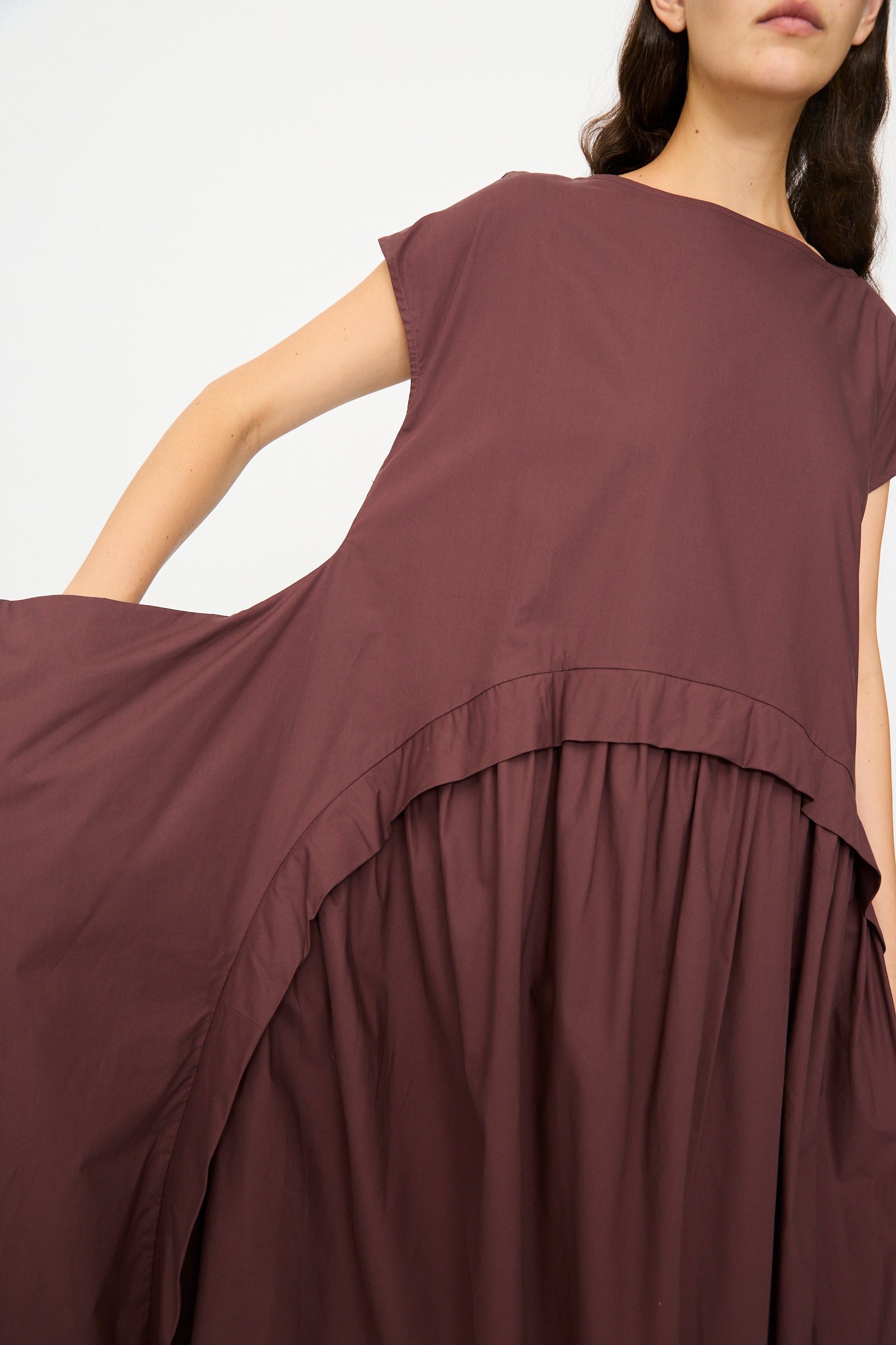 A woman wears the Rachel Comey Beau Dress in Merlot—an organic cotton, loose-fit, sleeveless midi dress with a round neckline and gathered waist.