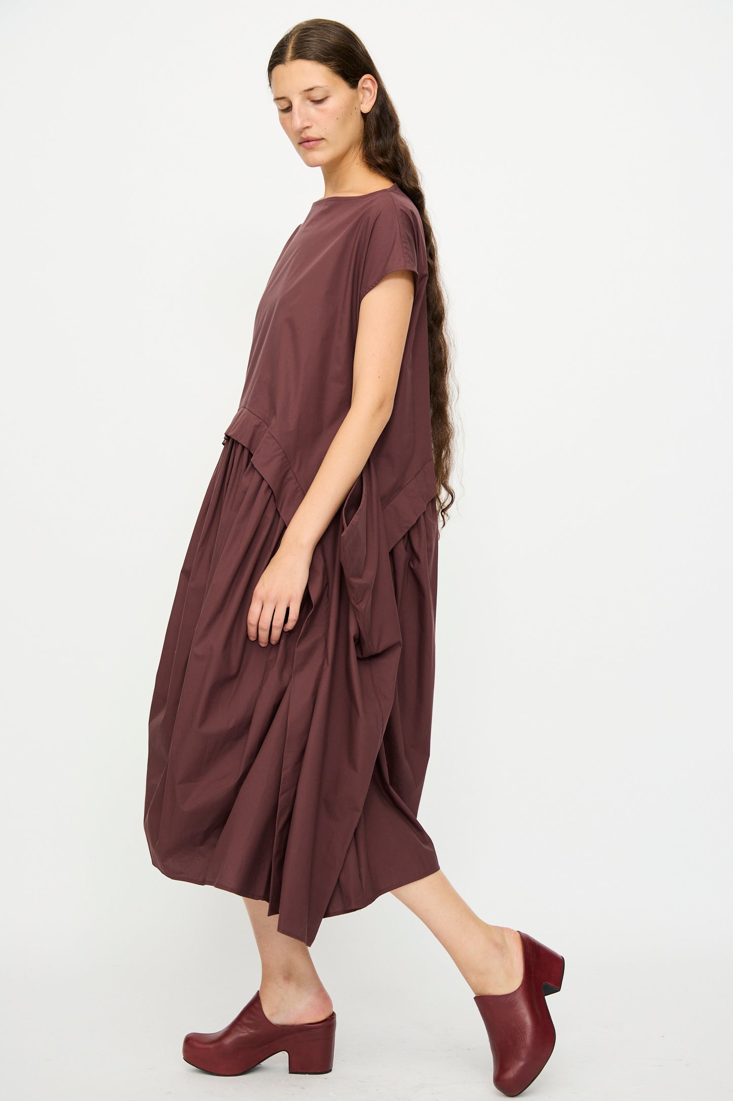 A woman with long brown hair models the Rachel Comey Beau Dress in Merlot, paired with matching platform shoes, against a plain white background.