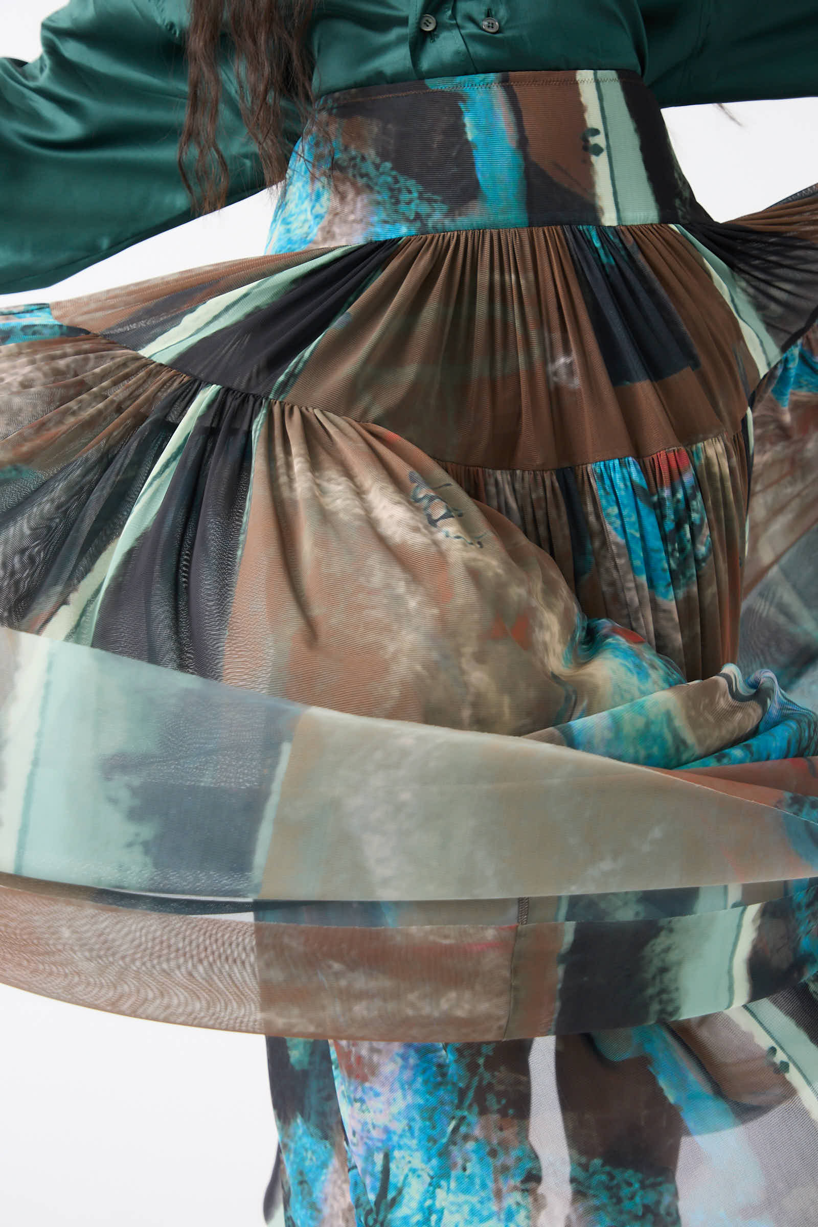 Close-up of a person wearing Rachel Comey's Brush Print Mesh Flock Skirt in Brown, showcasing its flowing, translucent fabric and tiered construction with colorful, multi-patterned designs featuring abstract brush prints in green, blue, and brown.