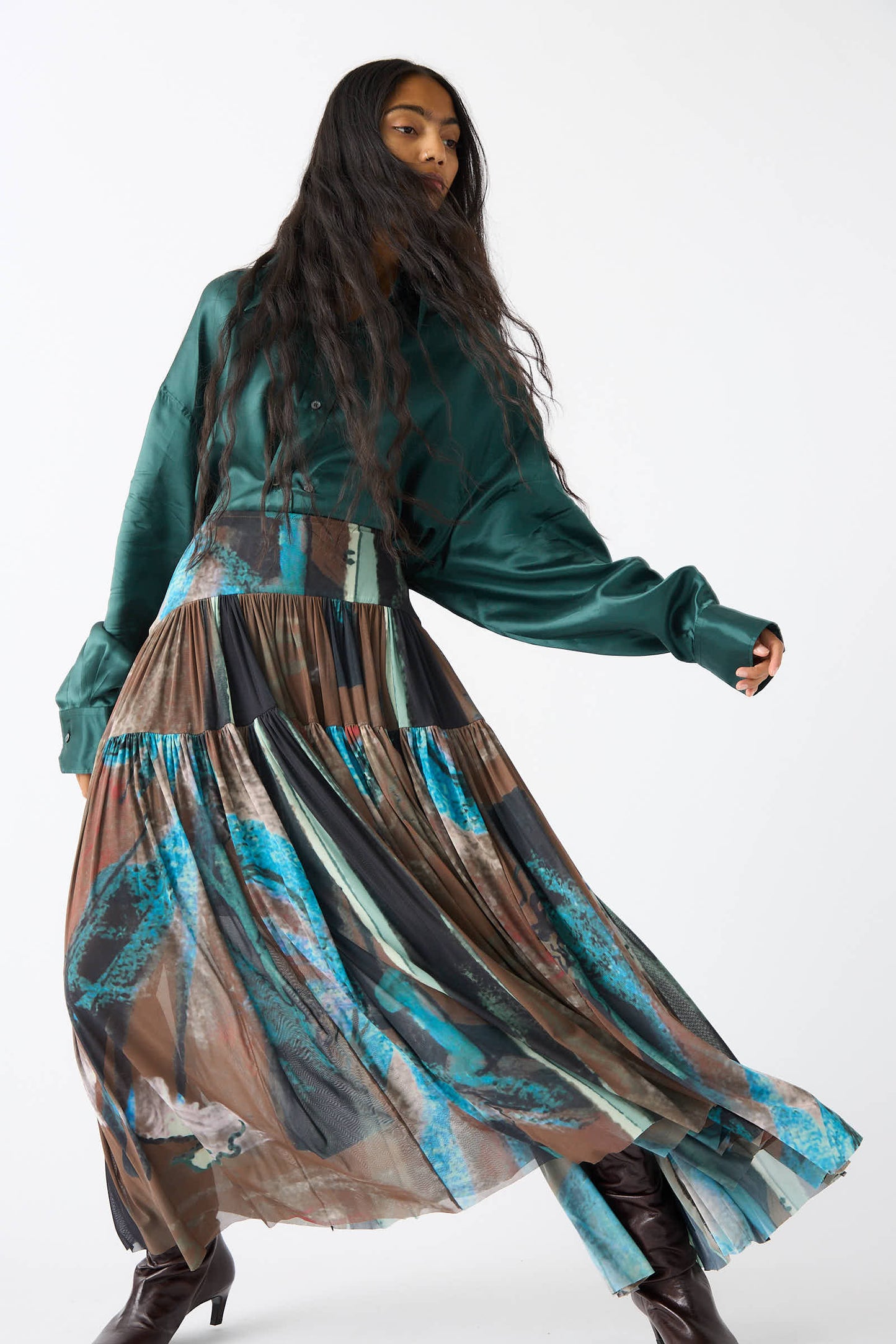 A person with long hair is posing against a plain white background, wearing a flowing Rachel Comey Brush Print Mesh Flock Skirt in brown and a green blouse.