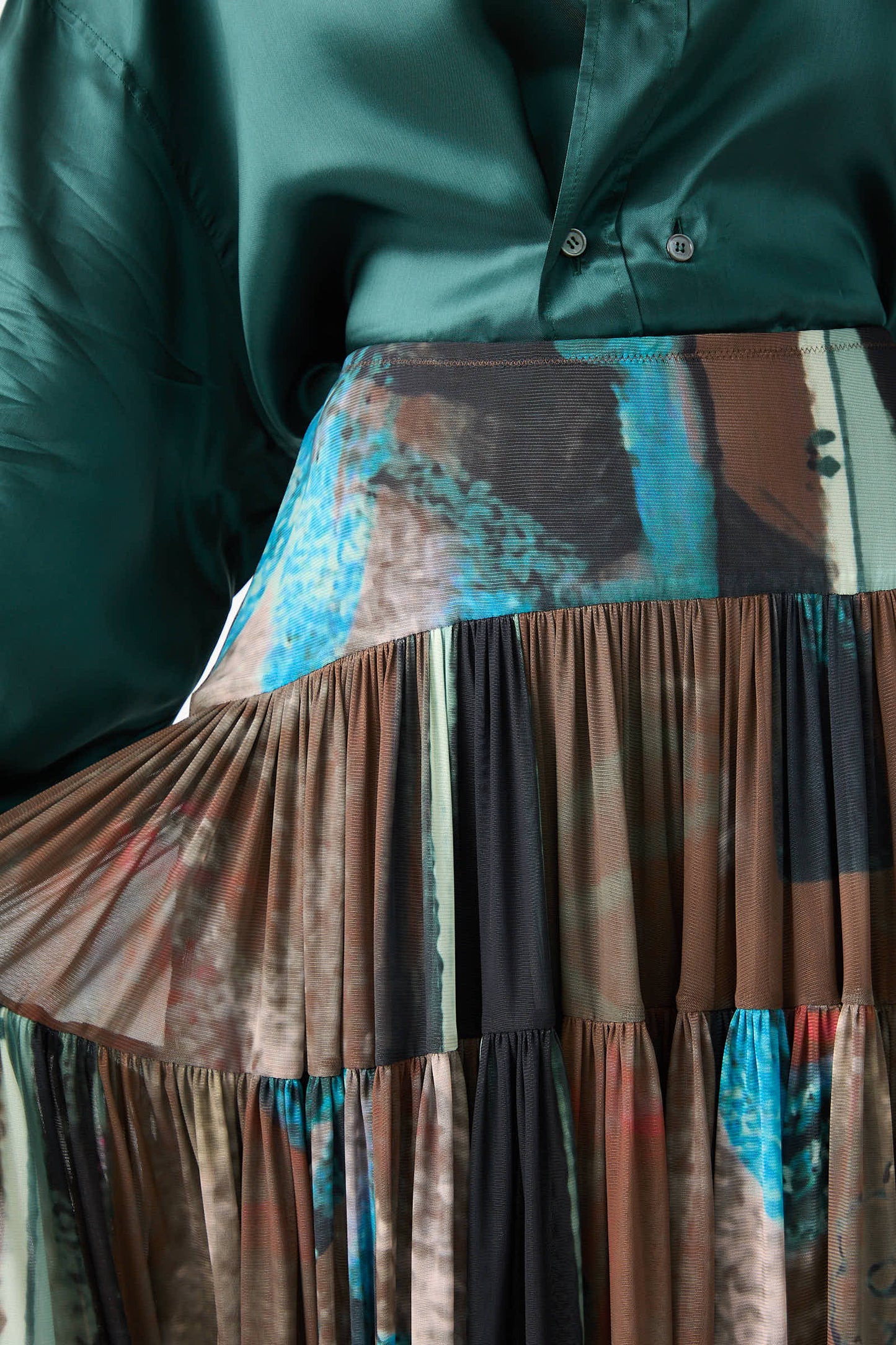 A close-up of a person wearing a buttoned green blouse paired with the Brush Print Mesh Flock Skirt in Brown by Rachel Comey, featuring abstract patterns in blue, brown, and black.