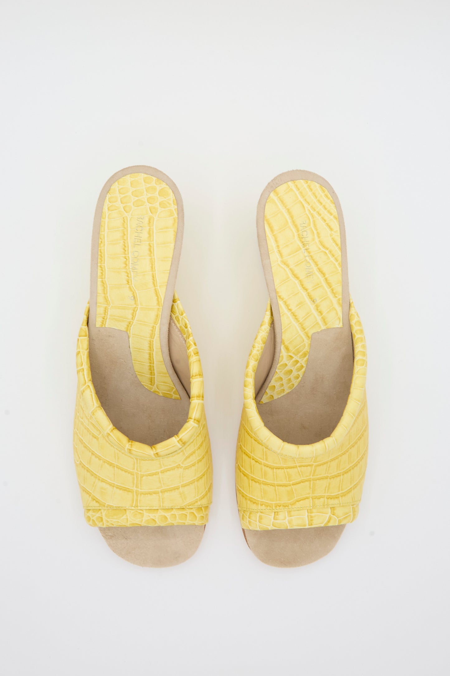 A pair of Bully Mule in Banana by Rachel Comey, featuring a yellow crocodile-patterned open-toe slip-on design with beige soles and a subtle snakeskin texture, shown from above against a white background.