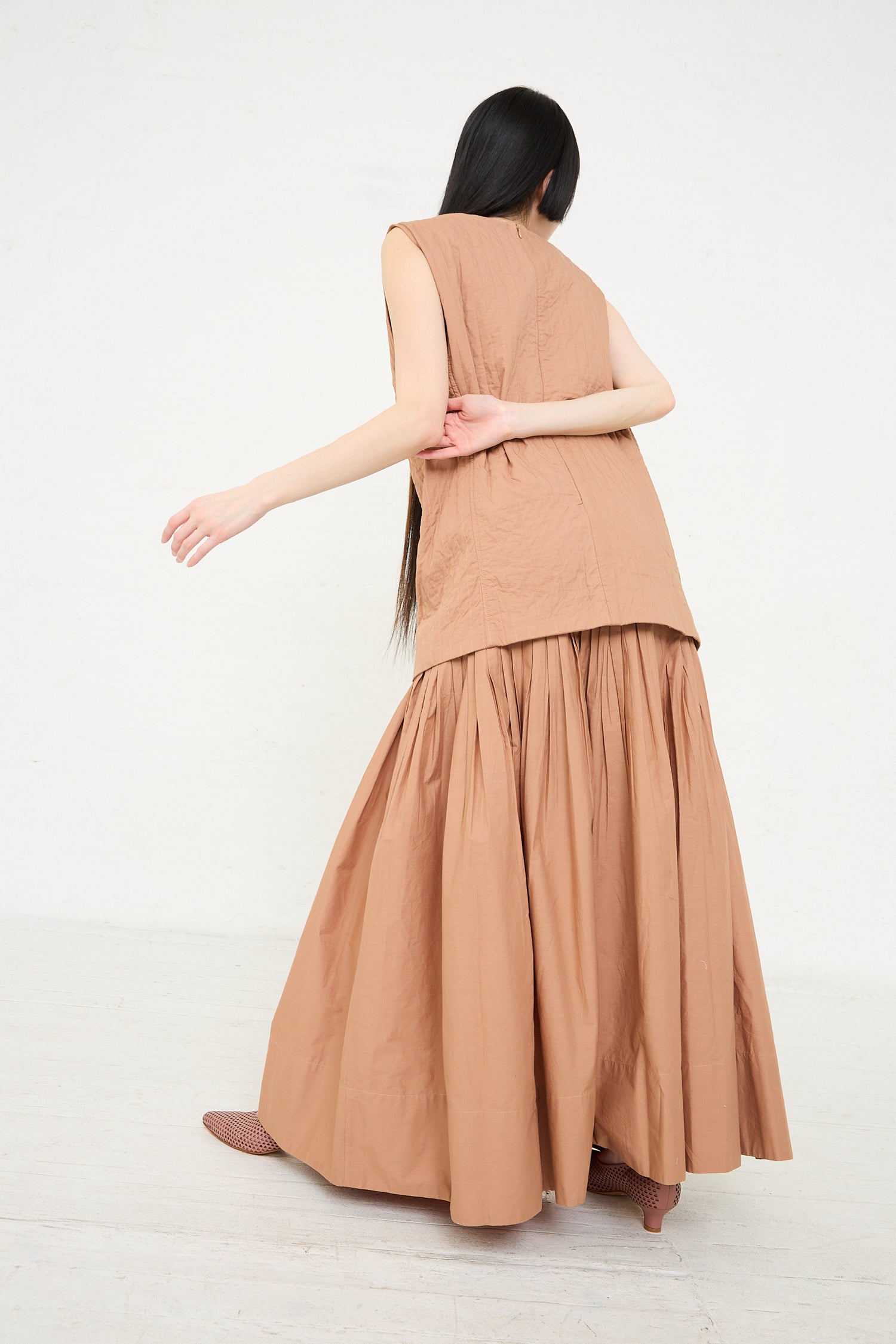 A woman seen from behind wearing a Calin Dress in Camel by Rachel Comey, with her arm outstretched.