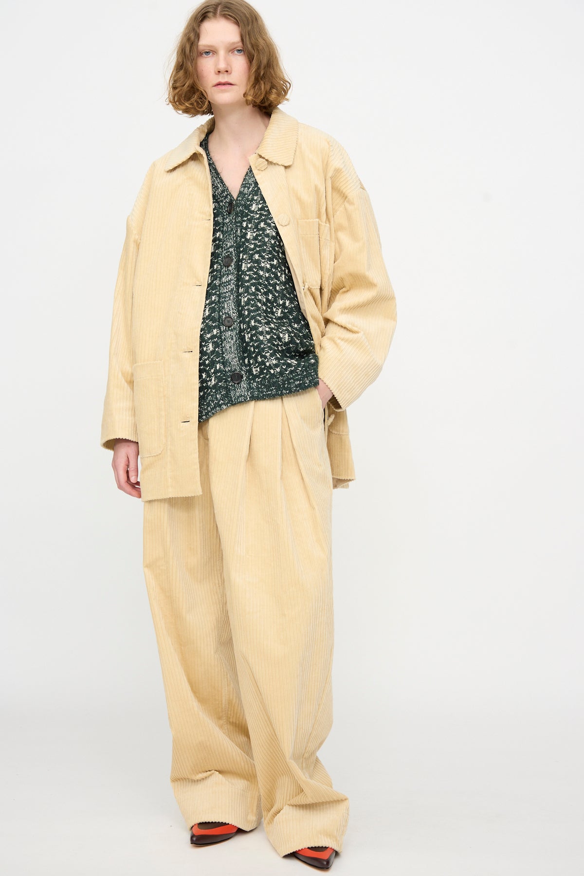 Model wears the Rachel Comey Chore Jacket in Dune—an oversized beige cotton corduroy style—paired with matching wide-leg pants, a dark green patterned top underneath, and black-and-orange shoes, set against a plain light background.