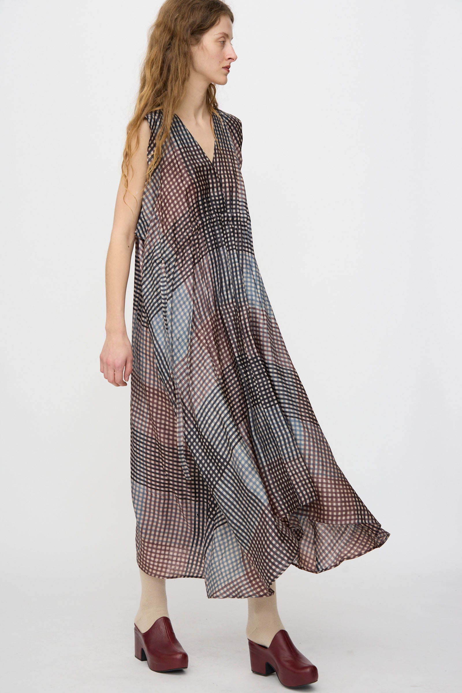 A woman wears the Rachel Comey Clement Dress in Juniper, paired with maroon shoes and beige socks, standing against a plain white background.