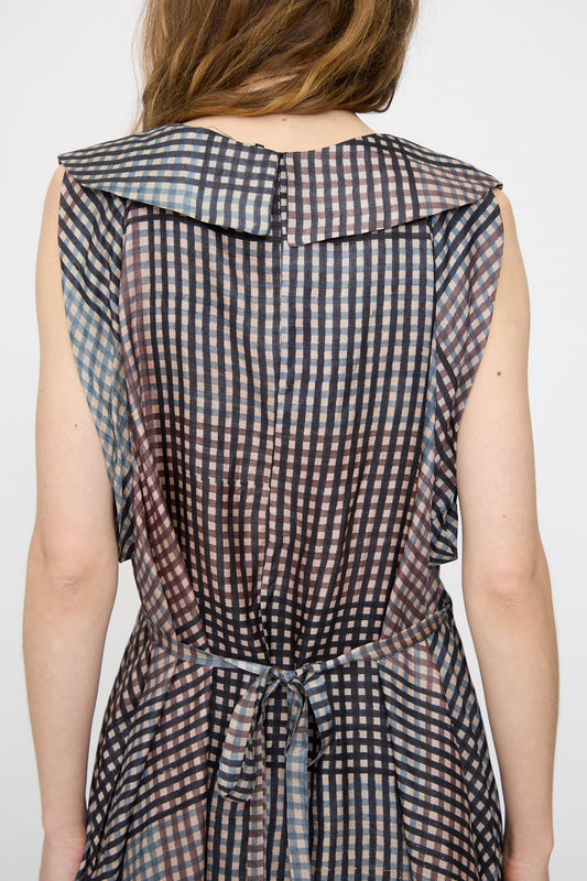 A person is seen from the back wearing the Rachel Comey Clement Dress in Juniper, featuring a black and white checkered block print, sailor-style collar, and waist tie.
