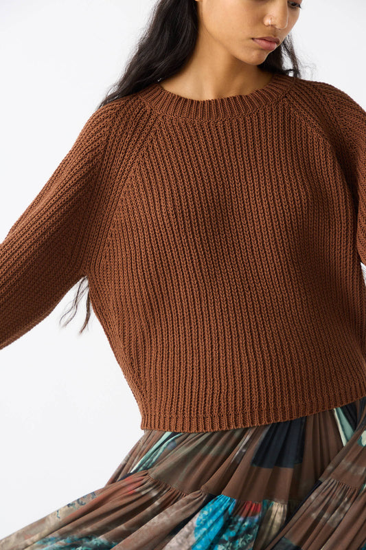 Person wearing the Rachel Comey Cotton Salla Sweater in Brown with balloon sleeves and a colorful patterned skirt, photographed from the shoulders to mid-thigh, facing slightly away from the camera.