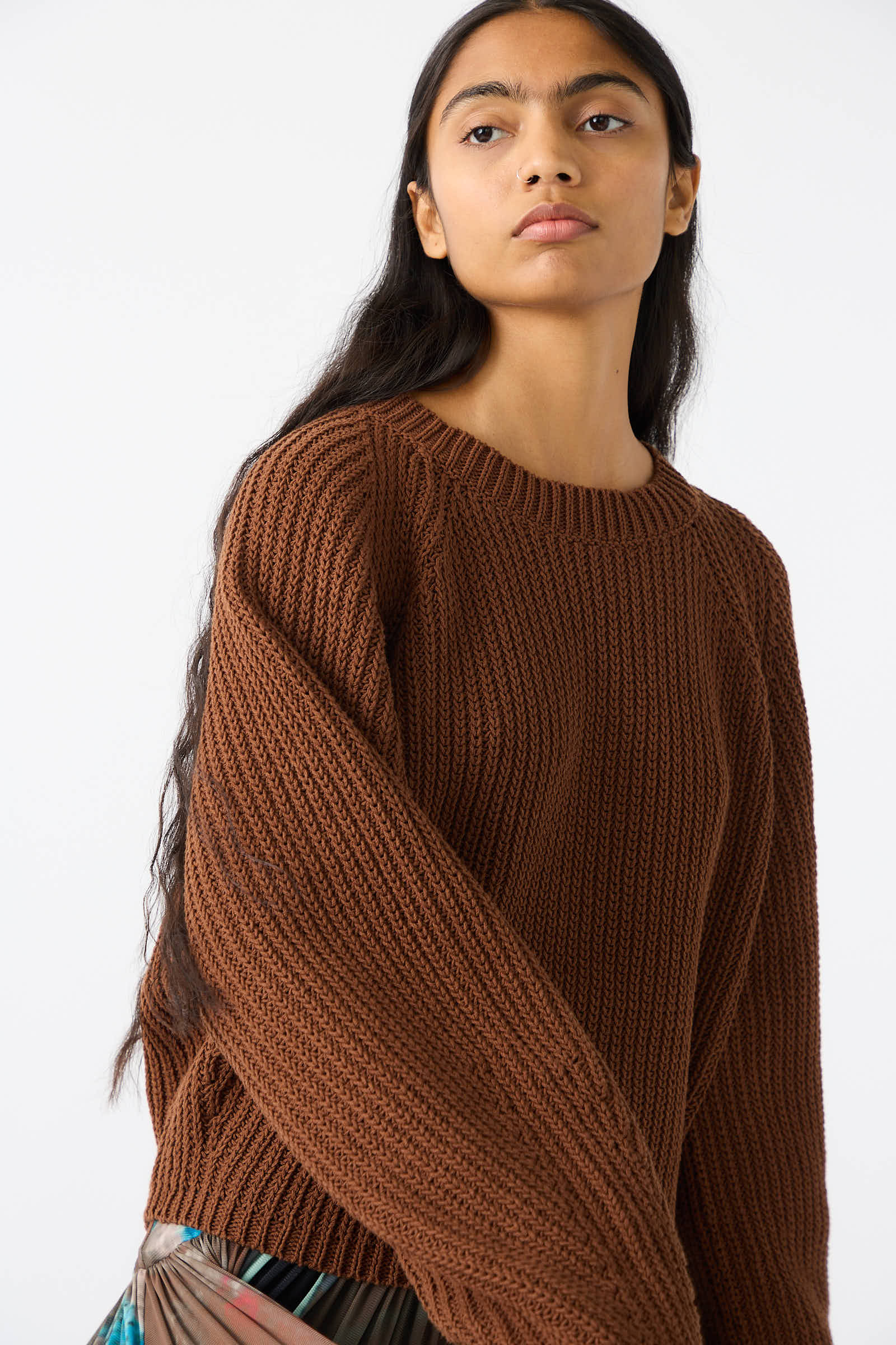 Person standing against a plain white background, wearing the Cotton Salla Sweater in Brown by Rachel Comey, featuring a cropped fit and balloon sleeves, looking slightly to the side.