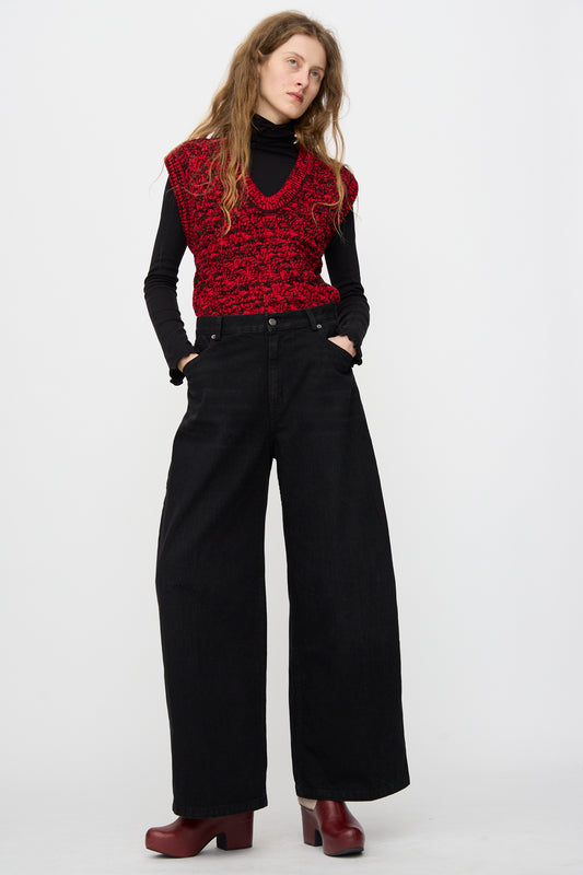A person stands with hands in pockets wearing the Rachel Comey Dottir Pant in Black, styled with a red knit vest, black turtleneck, and red platform shoes against a plain white background.