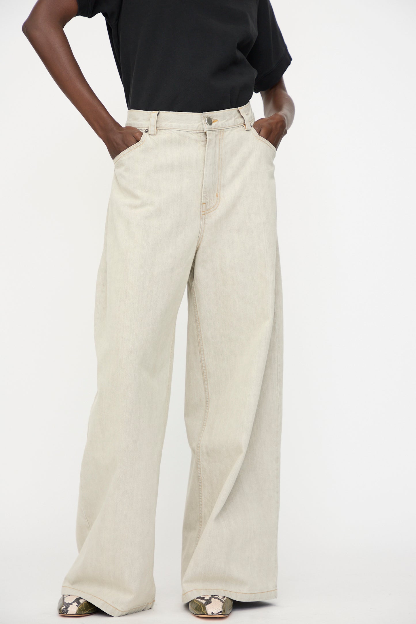 Person wearing a black t-shirt and Rachel Comey Dottir Pant in Khaki Wash, hands in pockets, standing against a plain white background.