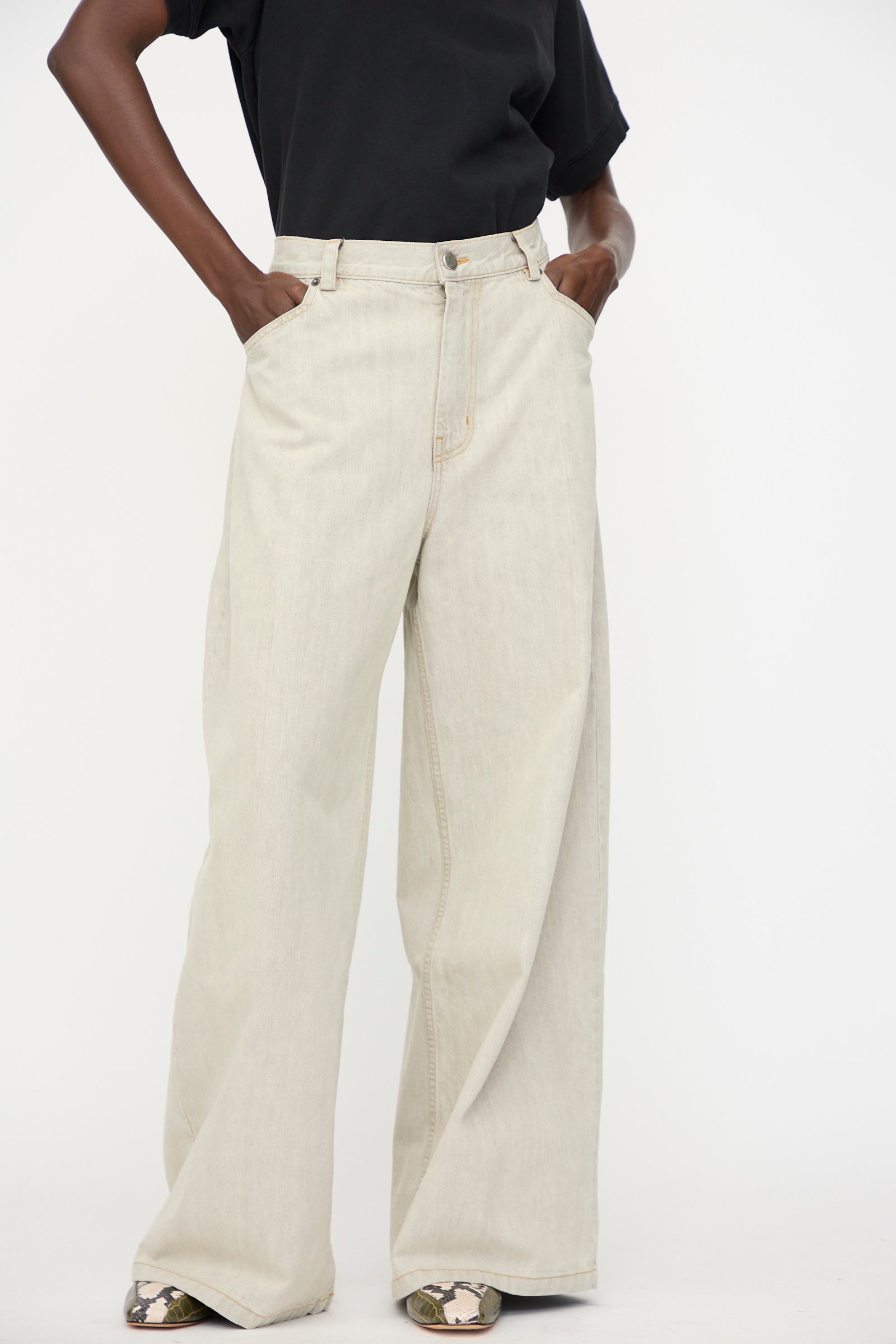 Person wearing a black t-shirt and Rachel Comey Dottir Pant in Khaki Wash, hands in pockets, standing against a plain white background.