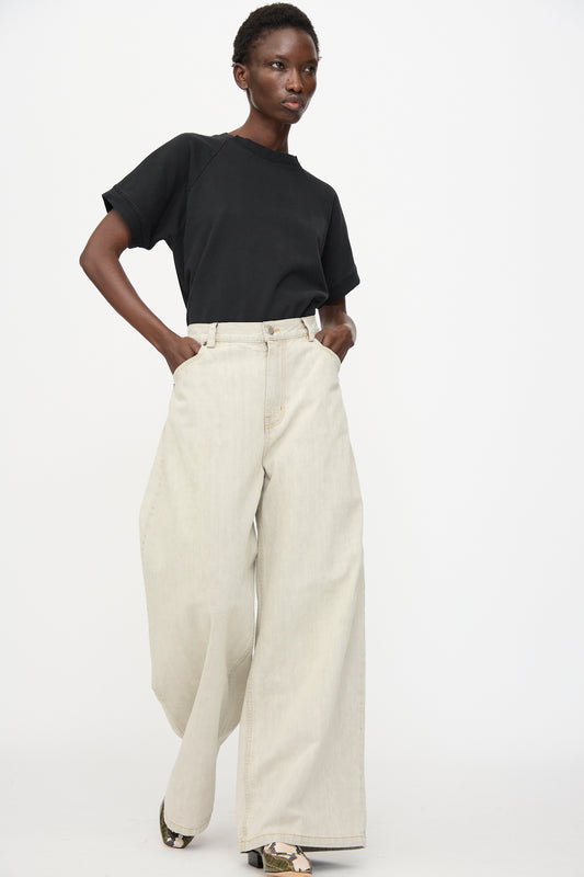 A person stands against a plain white background wearing a black t-shirt, patterned shoes, and the Rachel Comey Dottir Pant in Khaki Wash with one hand in their pocket.