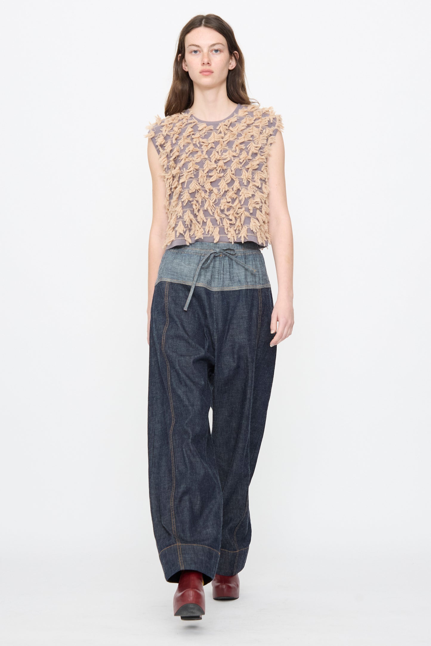 A model wears a sleeveless textured top, a gray belt, red ankle boots, and the Rachel Comey Ennu Pant in Indigo—wide-leg, relaxed-fit denim with visible seams—walking against a plain white background.