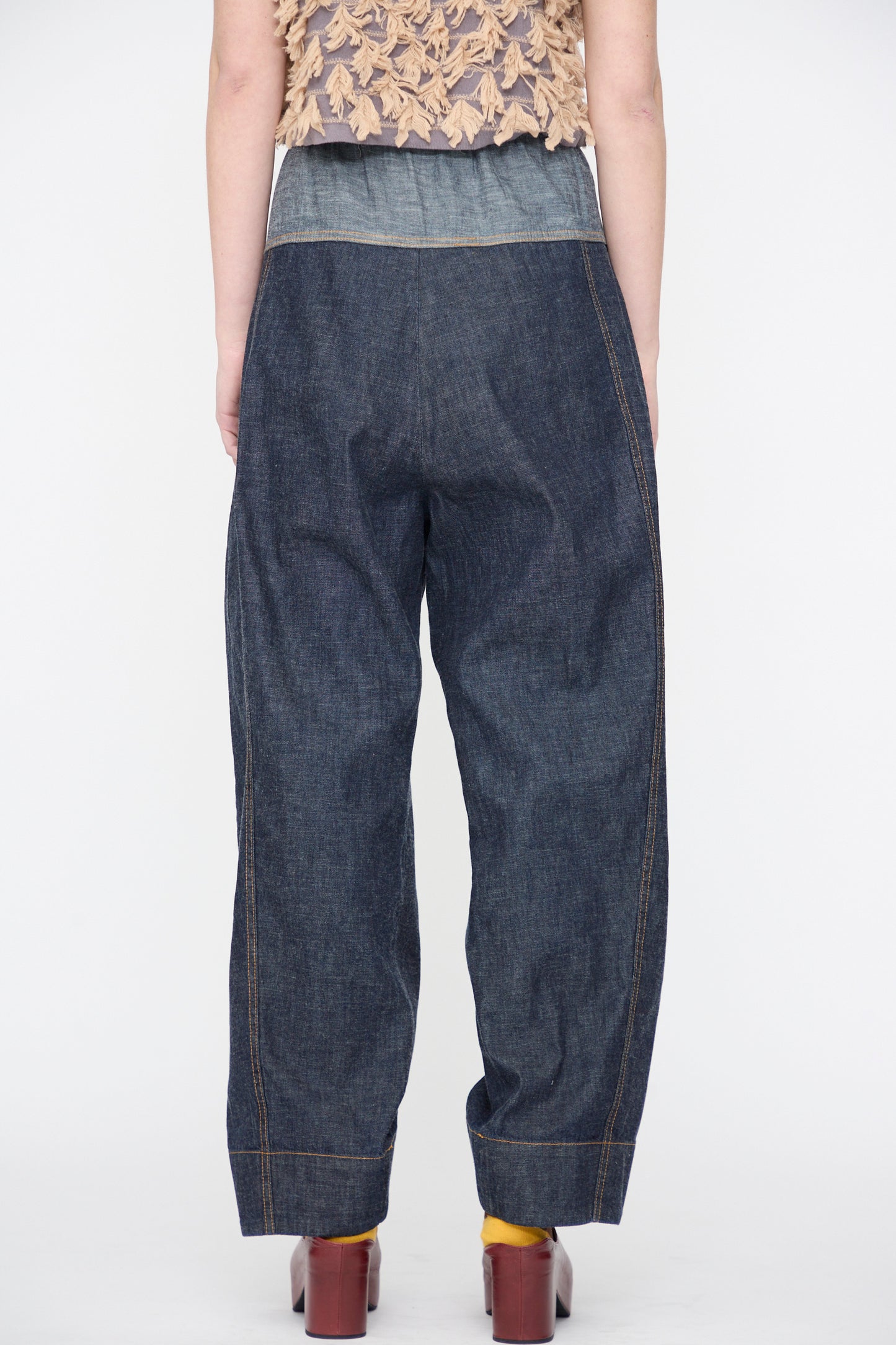 Person wearing the Rachel Comey Ennu Pant in Indigo, a beige textured top, yellow socks, and brown heeled shoes, photographed from the back against a plain white background.