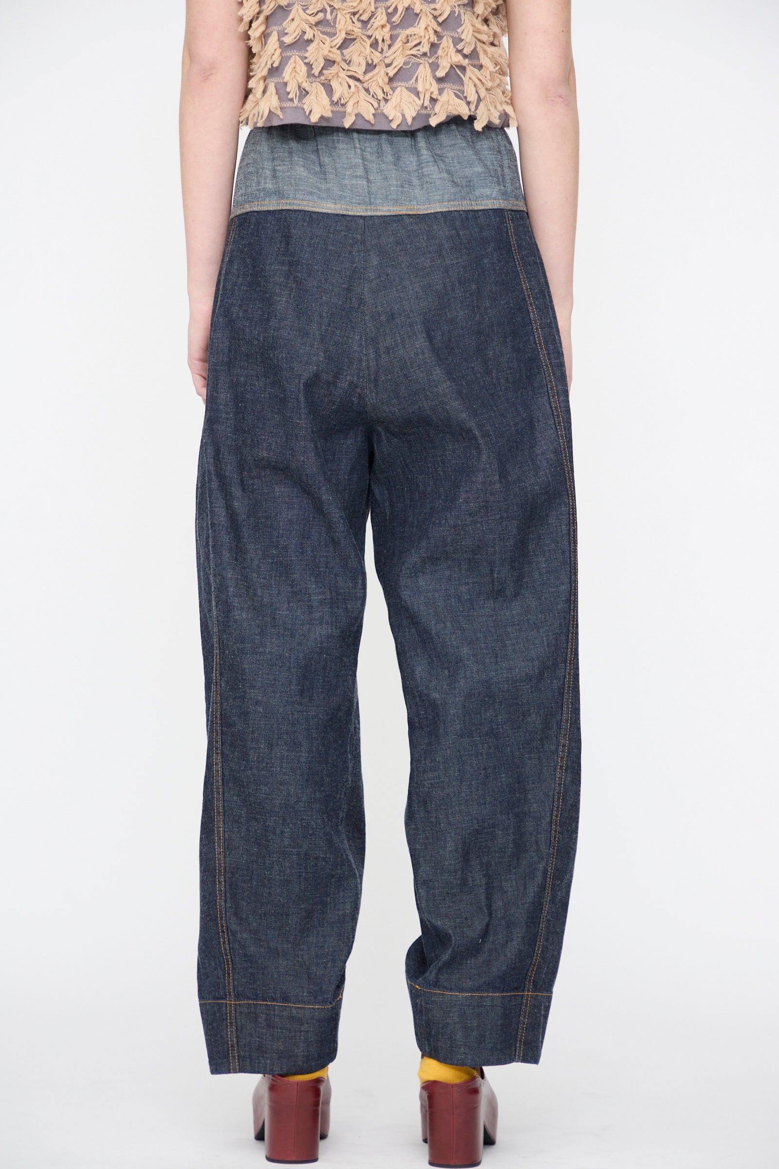Person wearing the Rachel Comey Ennu Pant in Indigo, a beige textured top, yellow socks, and brown heeled shoes, photographed from the back against a plain white background.