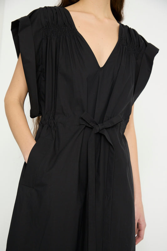 A model wearing Rachel Comey's Falls Dress in Black, a sleeveless maxi, designed with organic cotton, a V-neck, tie belt, and casual pocketed pose, against a white backdrop.