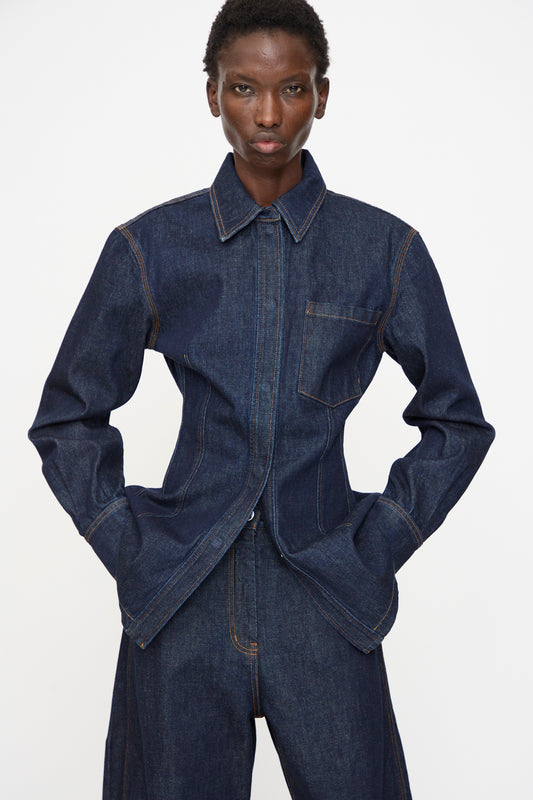 A person wears the Rachel Comey Filt Top in Raw Wash—a dark denim shirt—layered under a matching jacket and pants with tan stitching, standing against a plain white background with hands in pockets.
