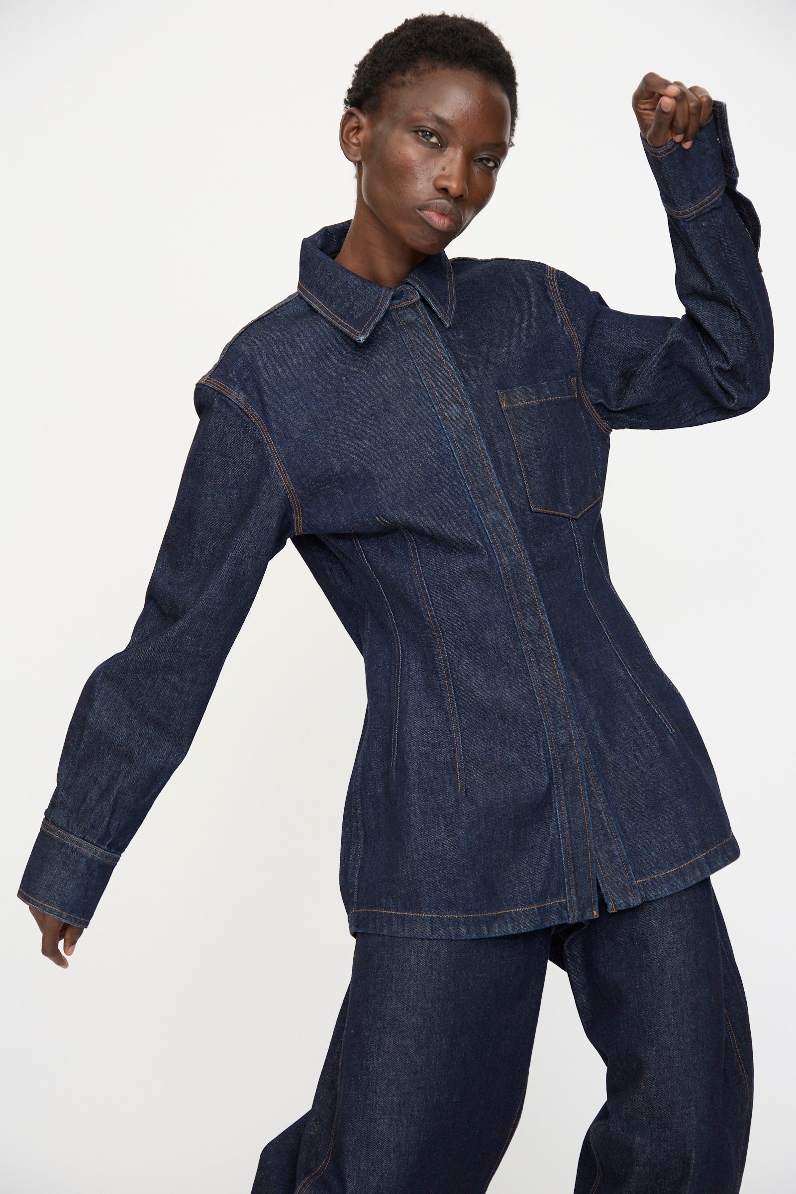 A person wears the Rachel Comey Filt Top in Raw Wash, posing with one arm bent and raised against a plain white background.