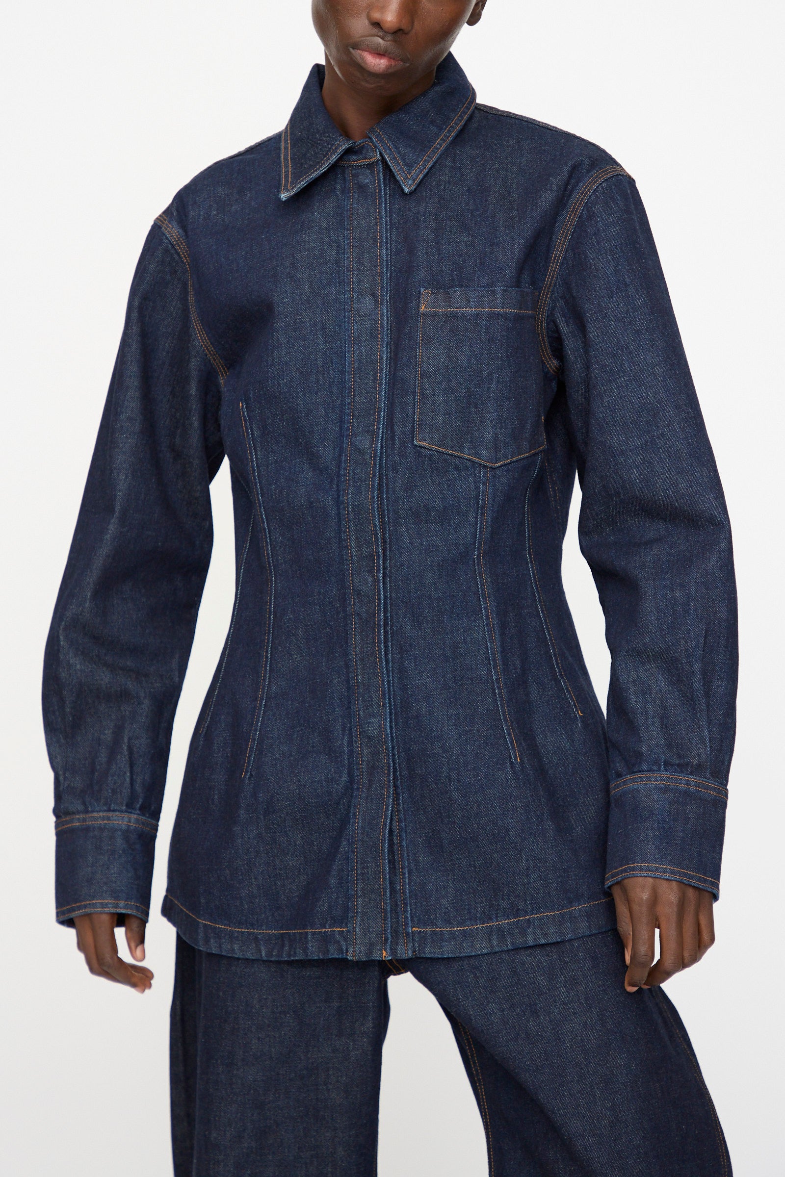 A person wears the Rachel Comey Filt Top in Raw Wash, a men’s relaxed fit long sleeve denim shirt jacket with contrast stitching and chest pocket, paired with matching denim pants against a plain background.