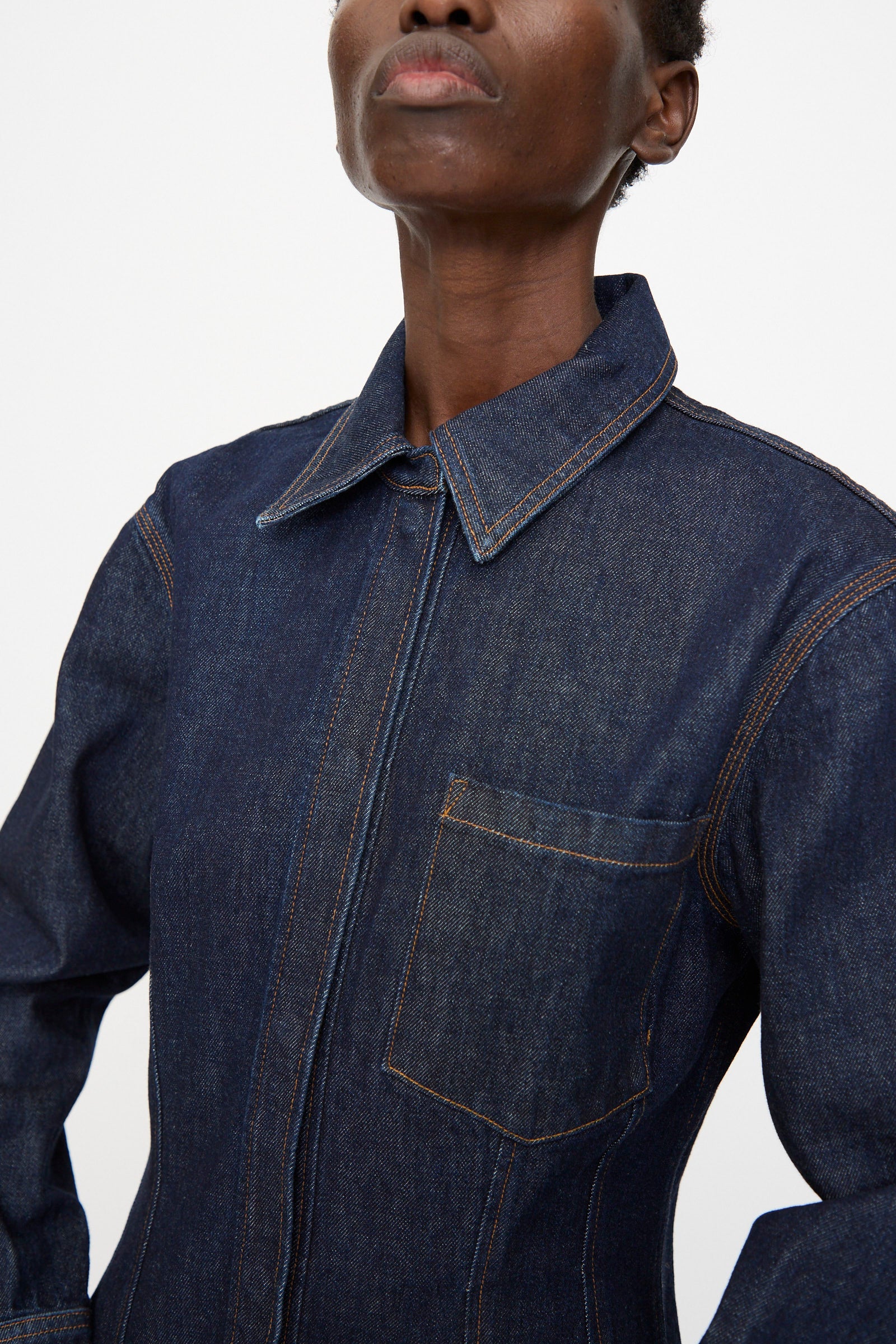 A person wearing the Rachel Comey Filt Top in Raw Wash, a dark blue long sleeve denim shirt with a front pocket and collar, shown from the shoulders up against a plain background.