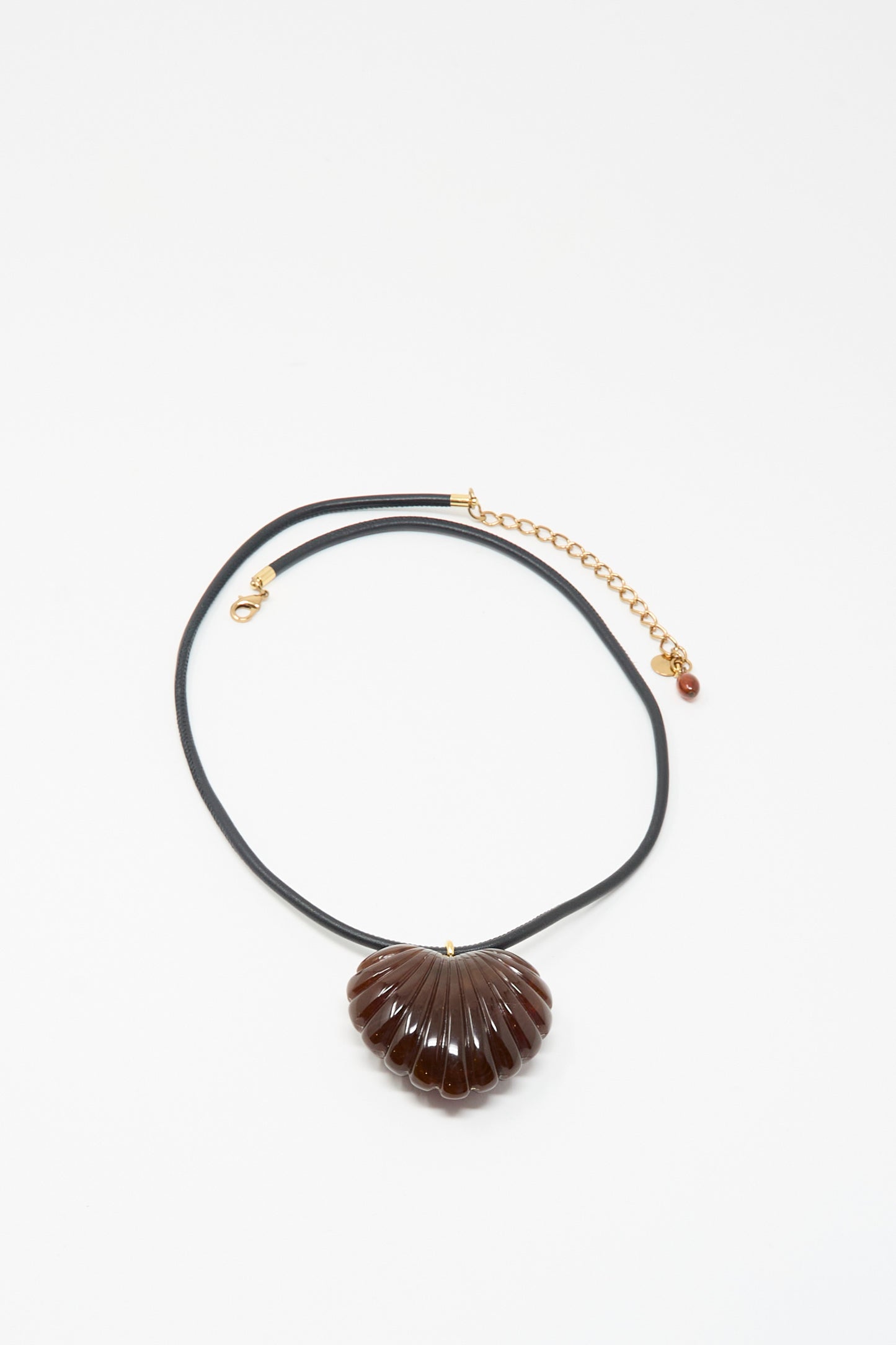 The Findon Necklace in Dark Tortoise by Rachel Comey features a black leather cord with a gold clasp and chain, accented by a brown, shell-inspired pendant for a unique touch of coastal elegance.