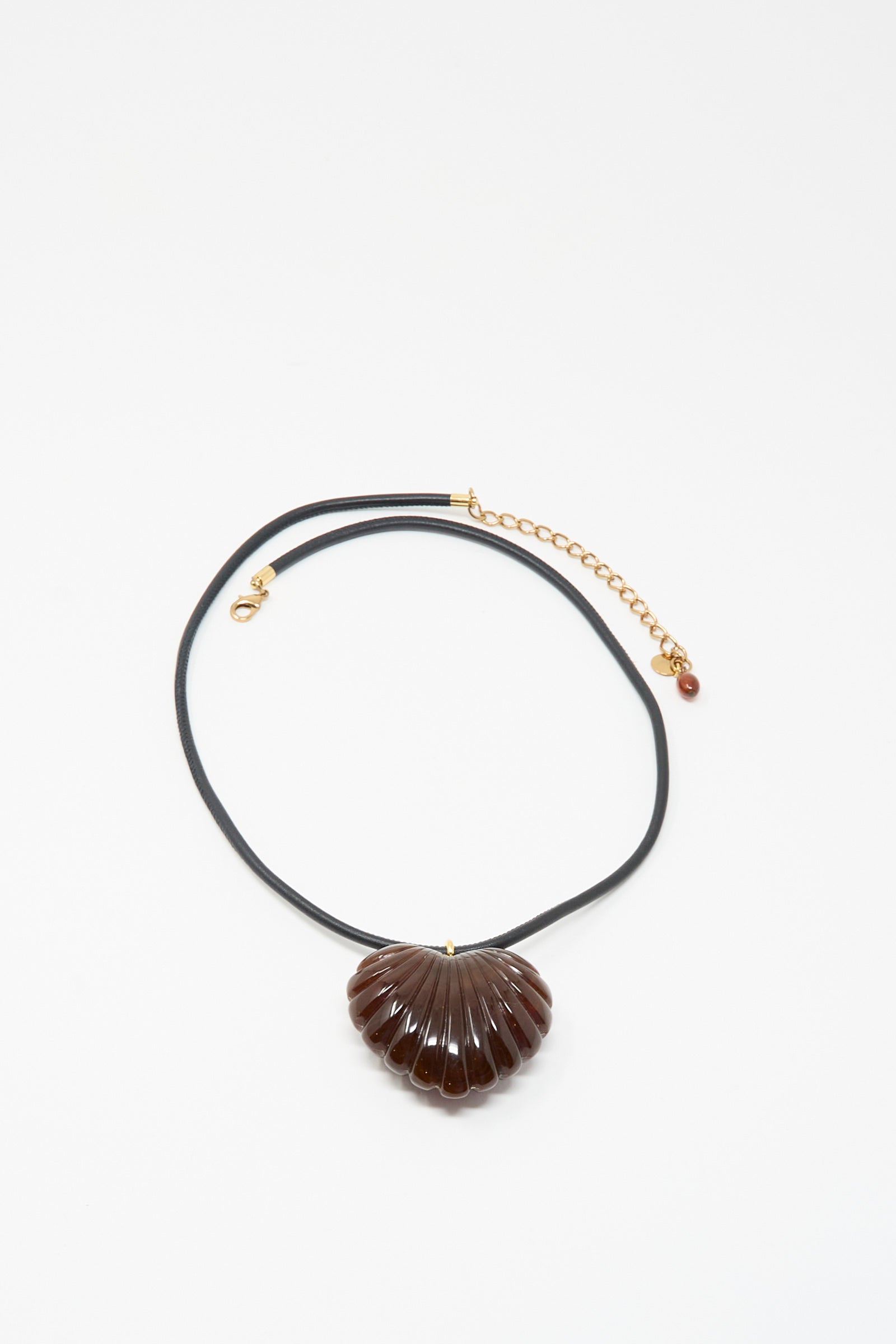 The Findon Necklace in Dark Tortoise by Rachel Comey features a black leather cord with a gold clasp and chain, accented by a brown, shell-inspired pendant for a unique touch of coastal elegance.