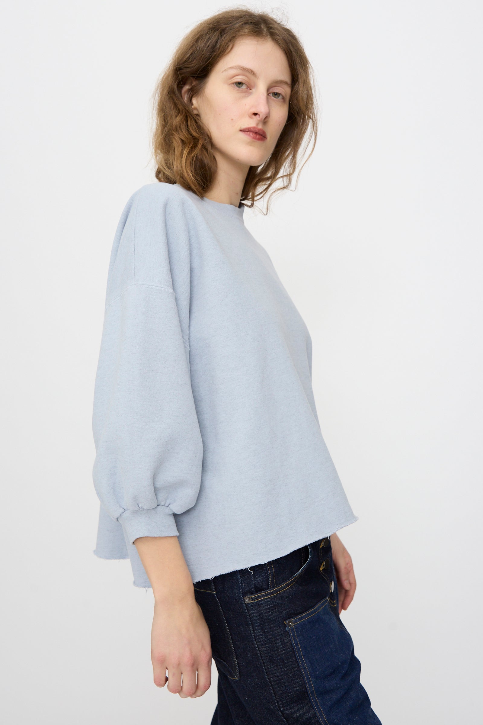 A woman wears the Rachel Comey Fond Sweatshirt in blue, featuring a distressed cotton blend and raw edge hem.