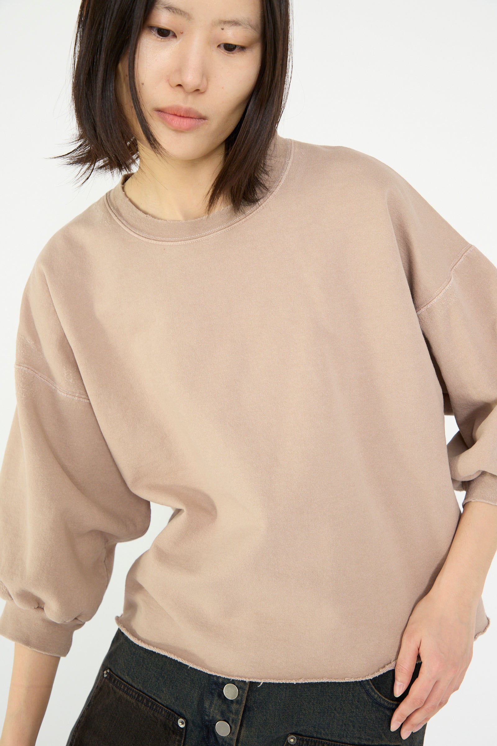 Wearing a Fond Sweatshirt in Buff by Rachel Comey and dark pants, a person looks down and to the side.