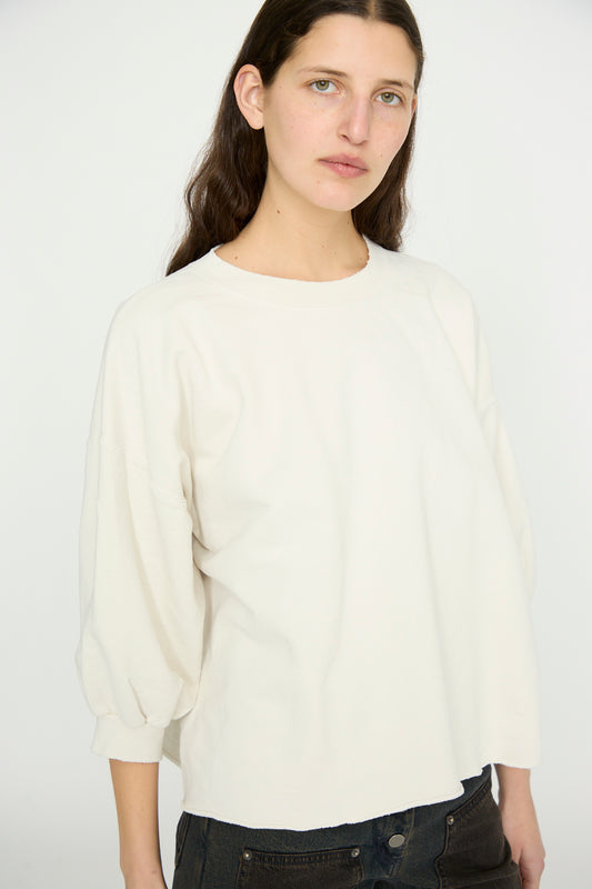 A person with long dark hair wears a Rachel Comey Fond Sweatshirt in Dirty White and black pants against a plain background.