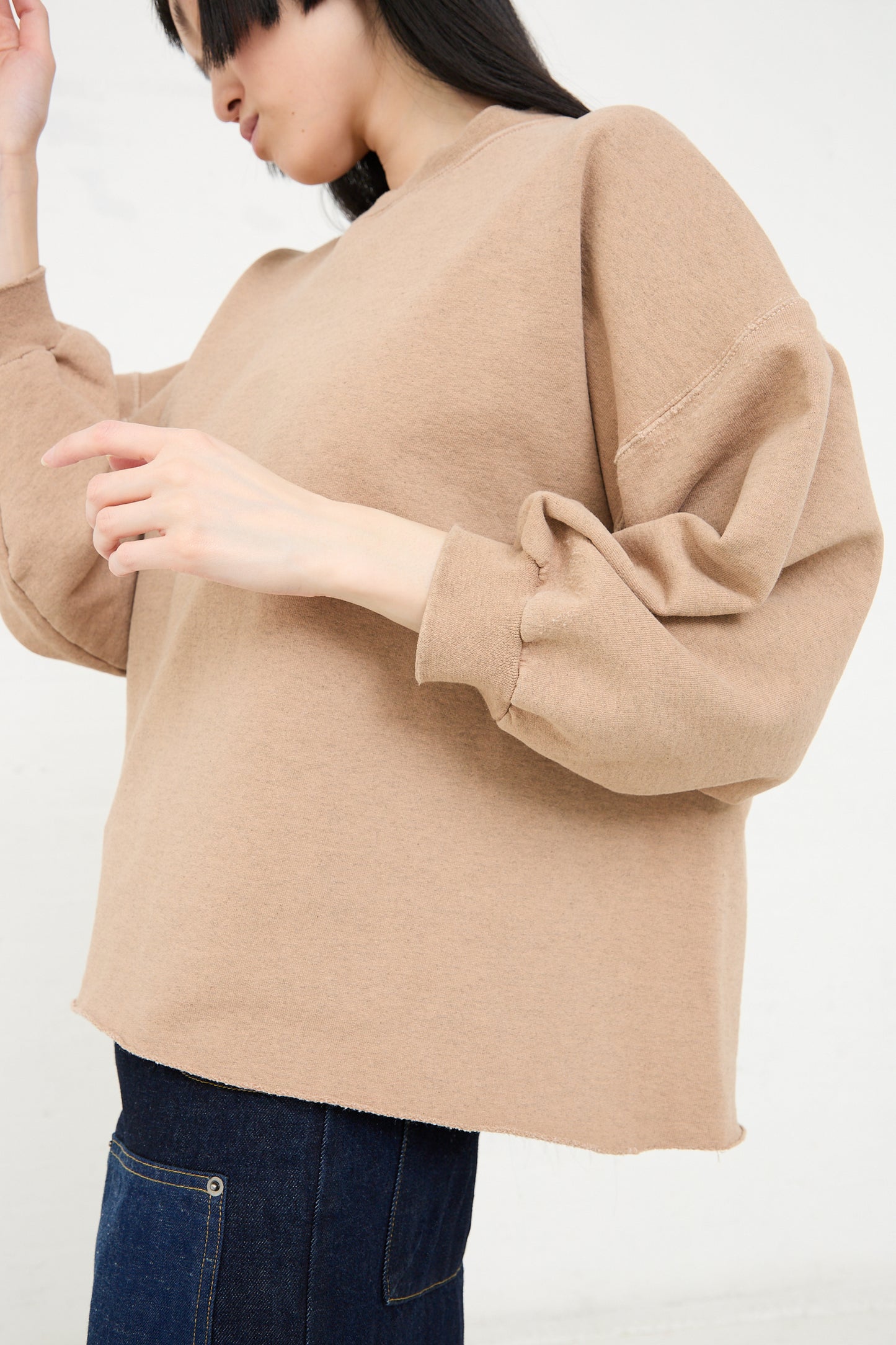 A person wearing an oversized, beige Rachel Comey sweatshirt with puffy sleeves and blue jeans.