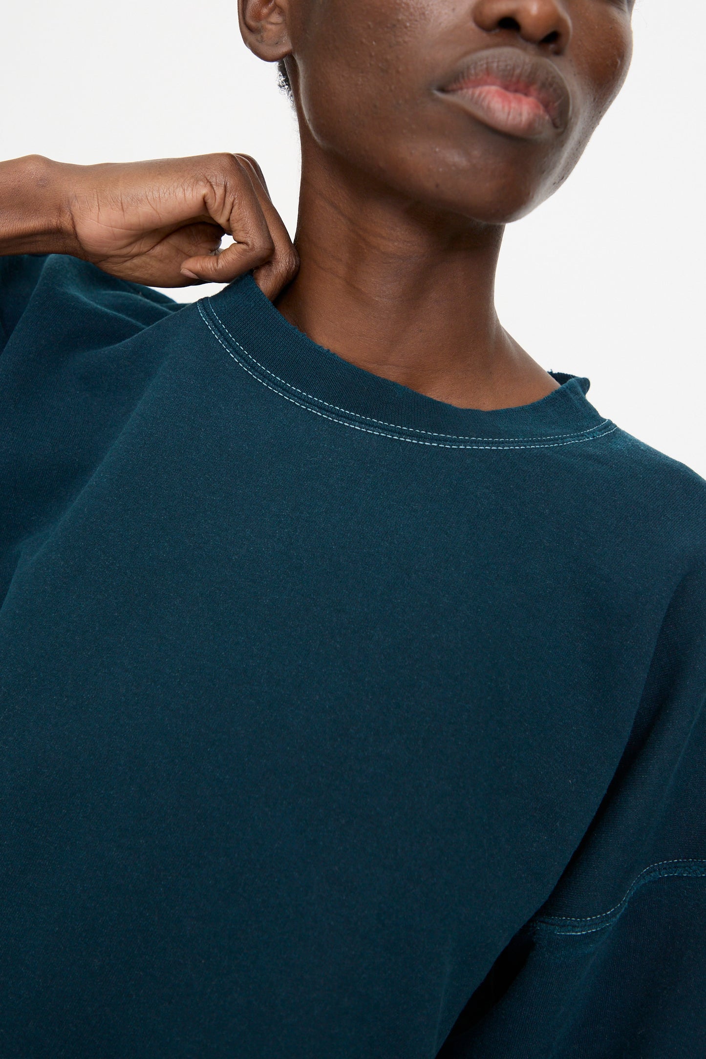 Model in the Rachel Comey Fond Sweatshirt in Teal, oversized and genderless, pulls at the collar with one hand. Shown from shoulders up against a plain background.