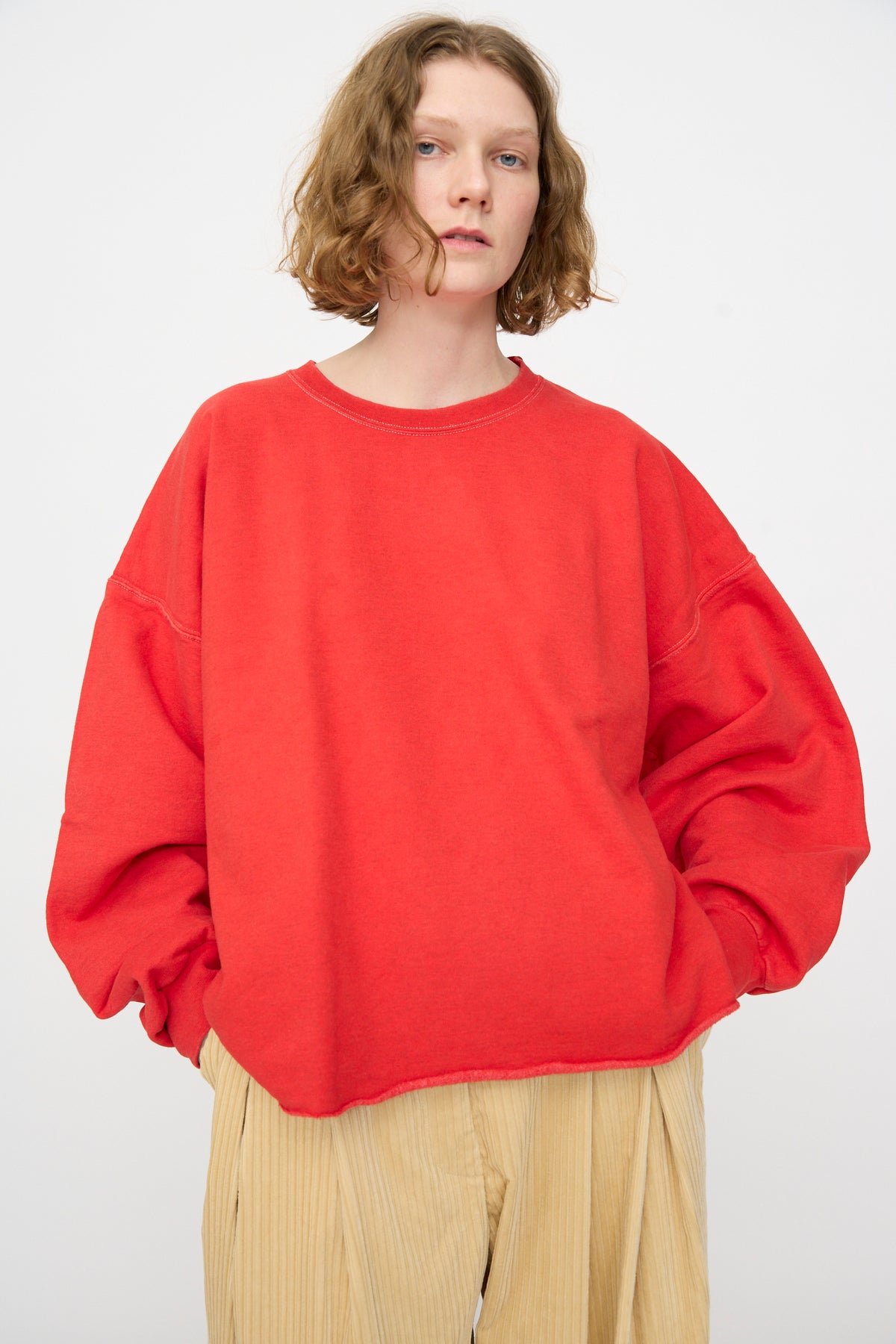 A person wearing the Rachel Comey Fonder Sweatshirt in Cherry, styled in an oversized and relaxed fit, paired with beige corduroy pants, stands against a plain light background.