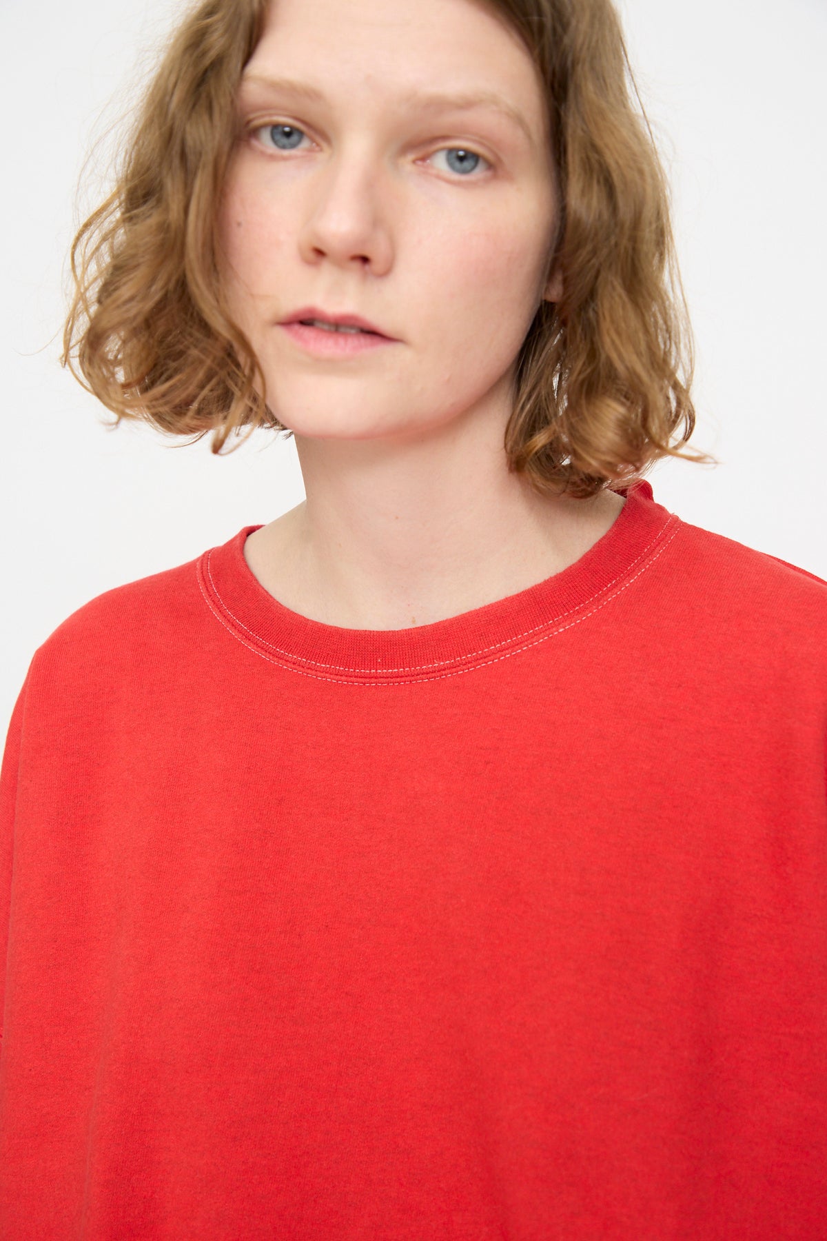 A person with short, wavy light brown hair is wearing the Rachel Comey Fonder Sweatshirt in Cherry, looking at the camera against a plain light background.