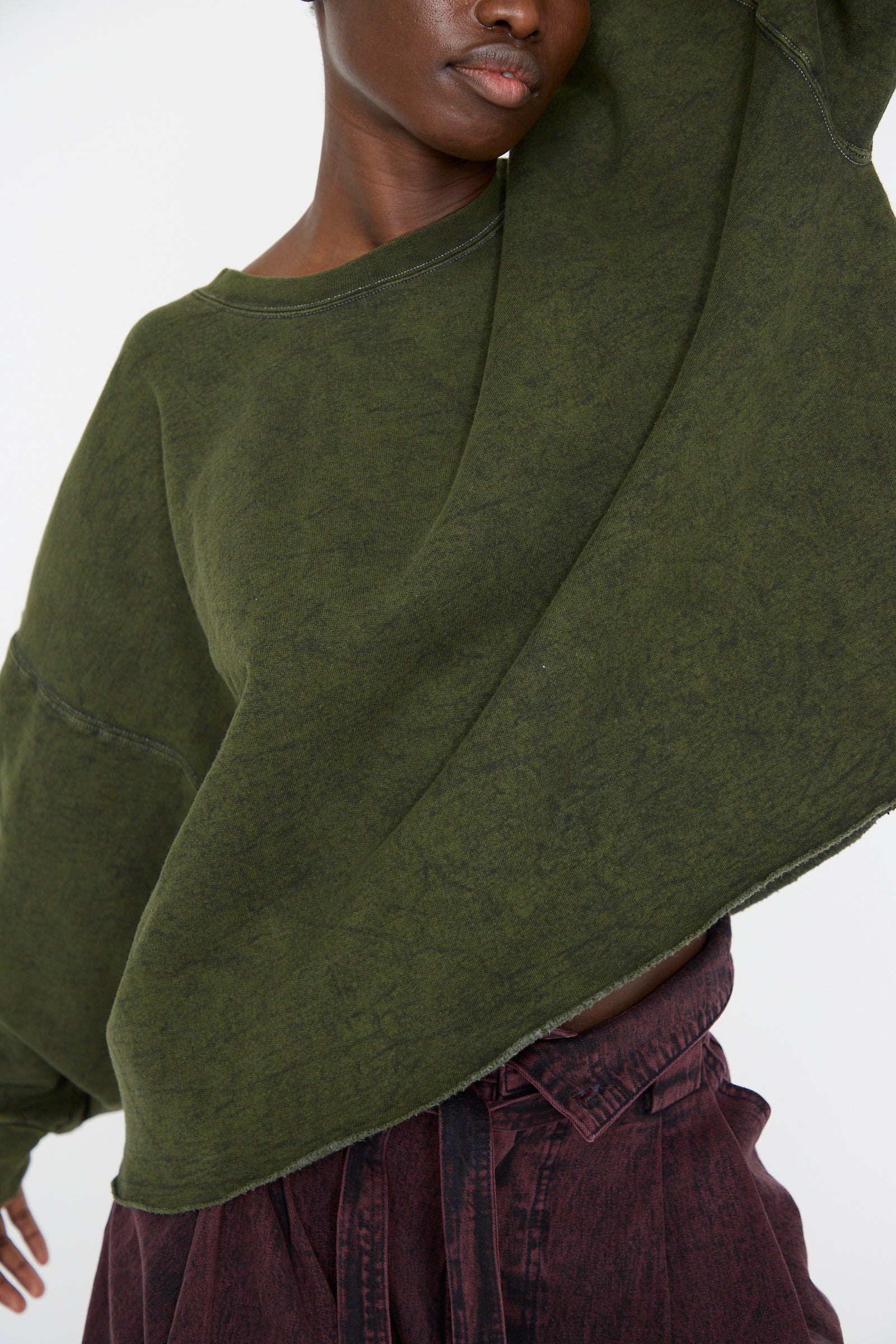 A woman wearing the Fonder Sweatshirt in Olive from Rachel Comey, featuring an oversized fit and crafted from a cotton blend fabric, raises her arm against a white background. 