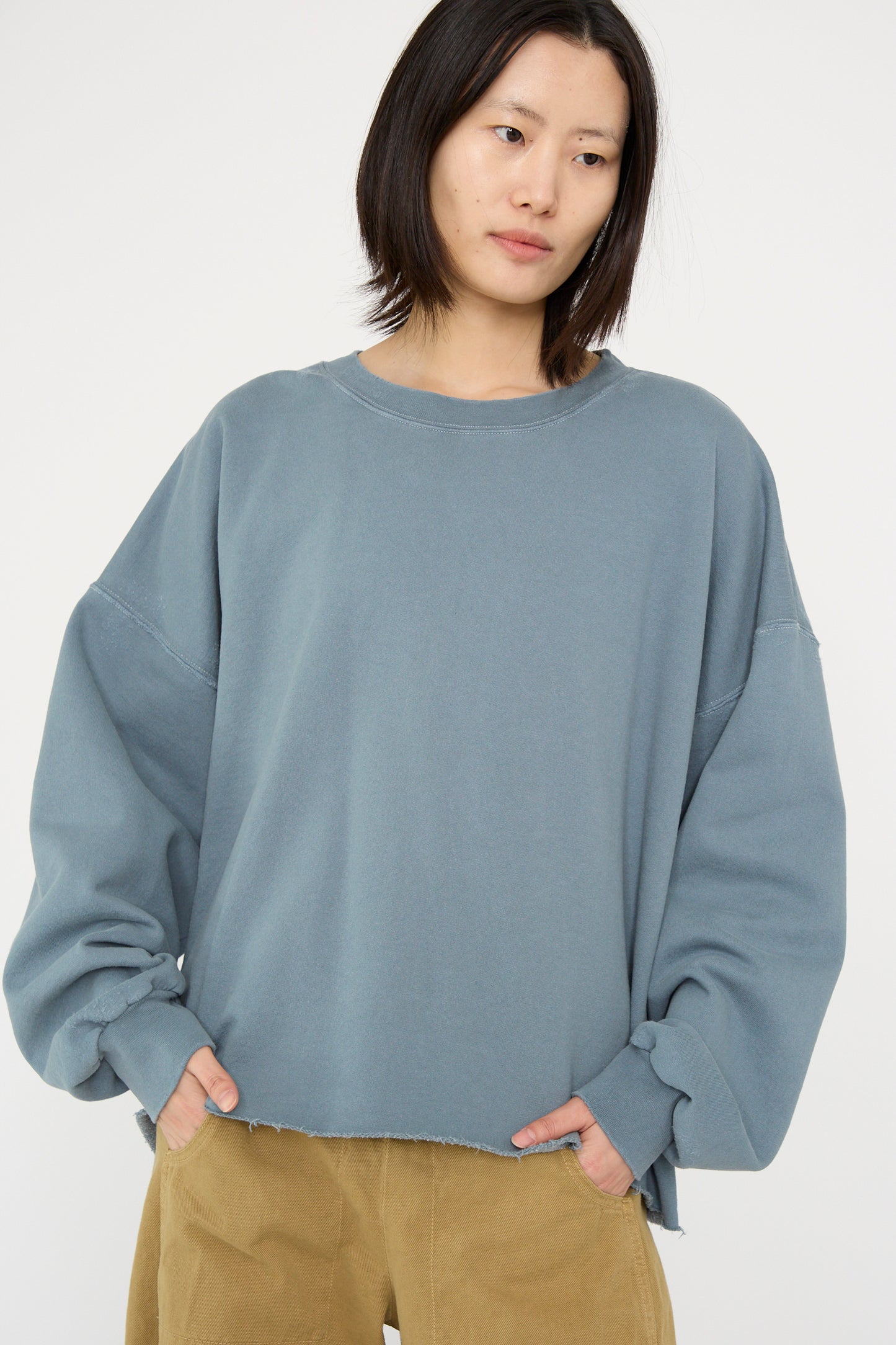 A person is wearing a Rachel Comey Fonder Sweatshirt in Petrol, featuring an oversized fit and a cozy cotton blend, paired with khaki pants, against a plain background.