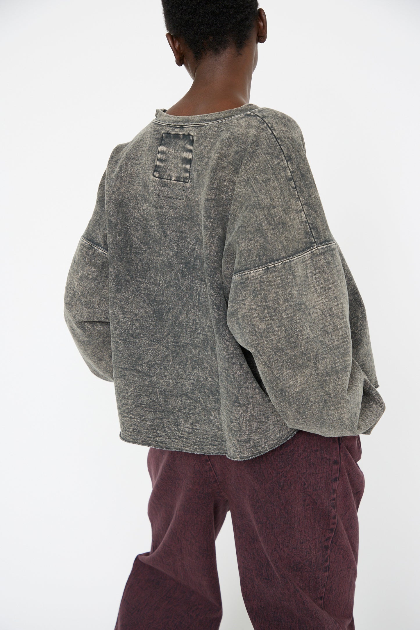 A woman is seen from behind, wearing the Fonder Sweatshirt in Smoky Hazelnut by Rachel Comey, featuring an oversized fit with wide sleeves, against a white background. 