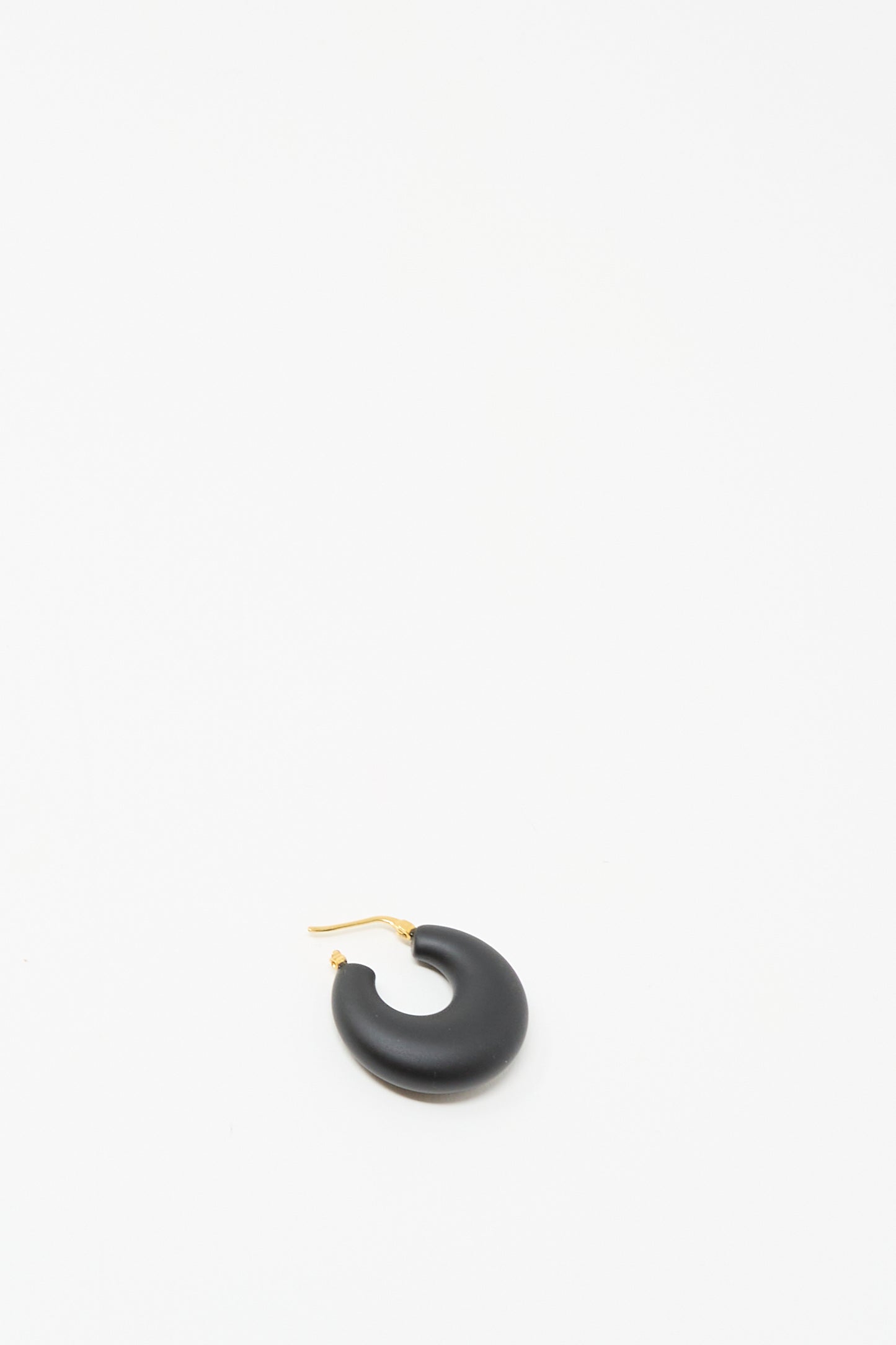 A single Grass Earring in Black Matte by Rachel Comey, featuring a chunky hoop and gold hinged fastening, is positioned near the center of a plain white background.